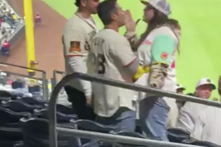 Three friends in casual attire chatting at a baseball stadium, with game visible below