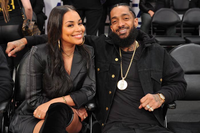 Lauren London and Nipsey Hussle smiling, seated close together at a music event. Both in stylish black attire
