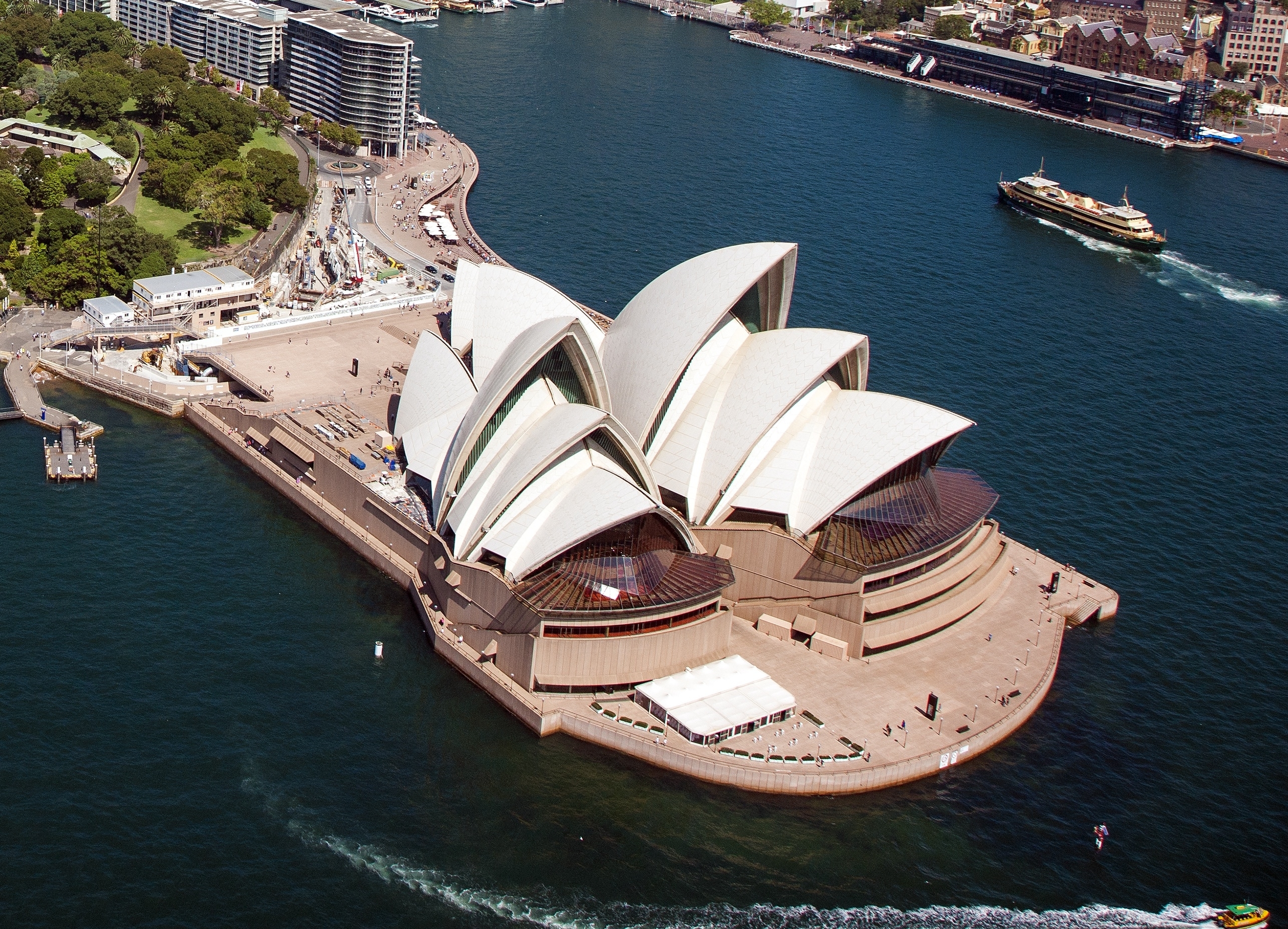 Aerial view of the Sydney Opera House beside the harbor, with nearby buildings and a boat on the water