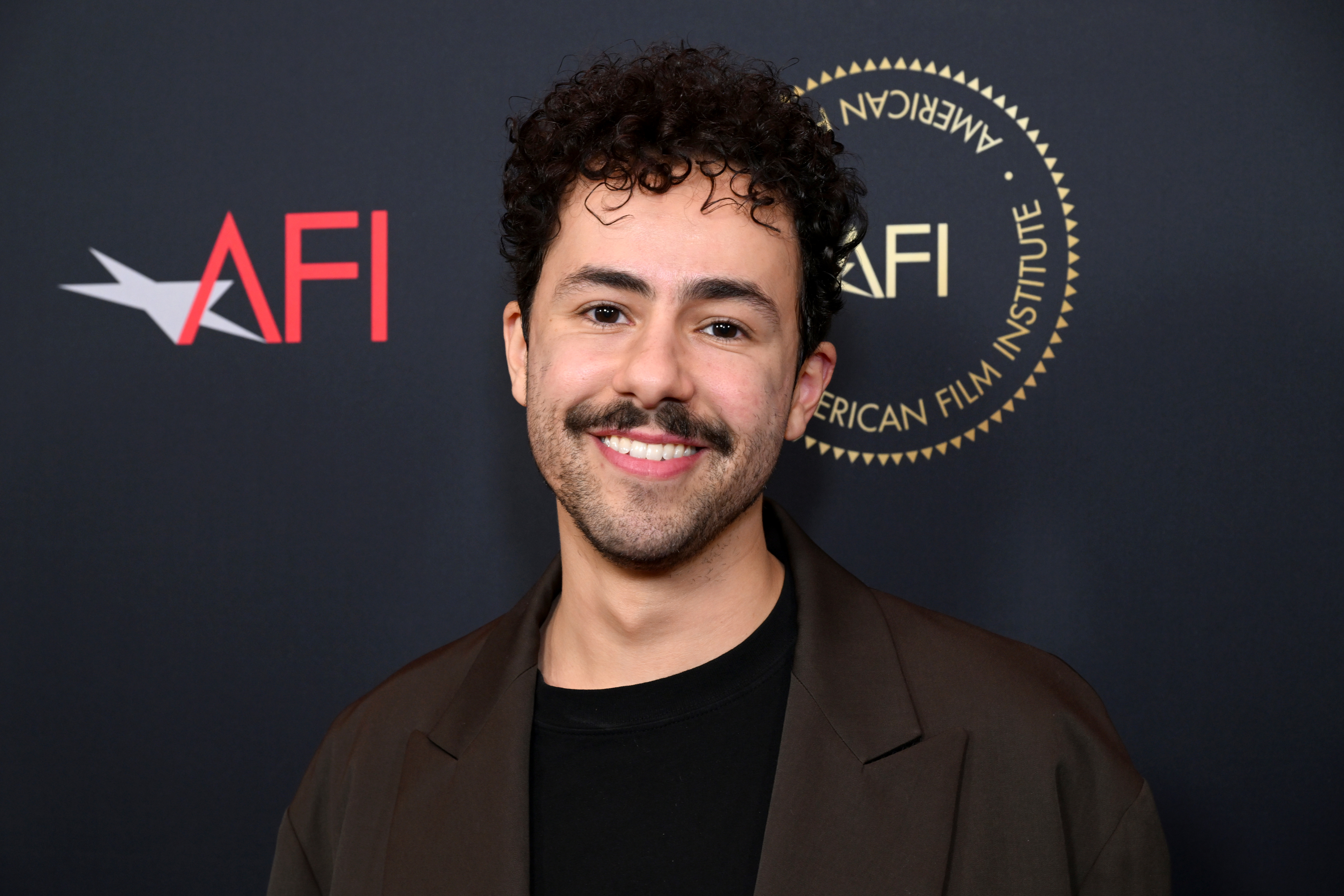 Man in a brown jacket and black shirt smiling at an AFI event