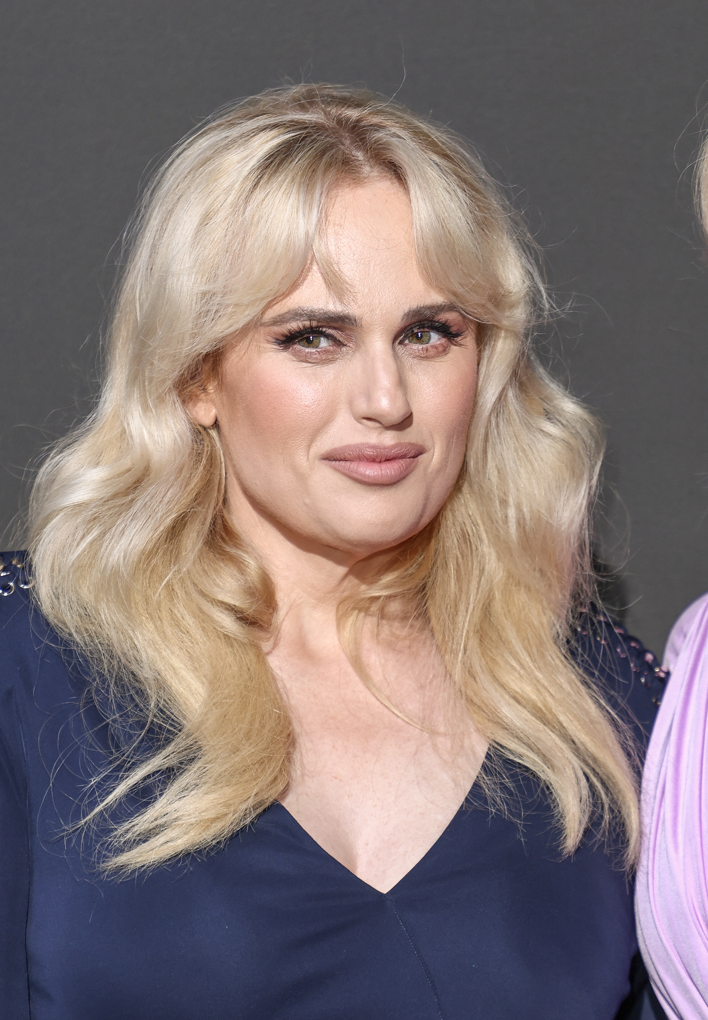 Rebel Wilson poses smiling in a navy outfit at an event