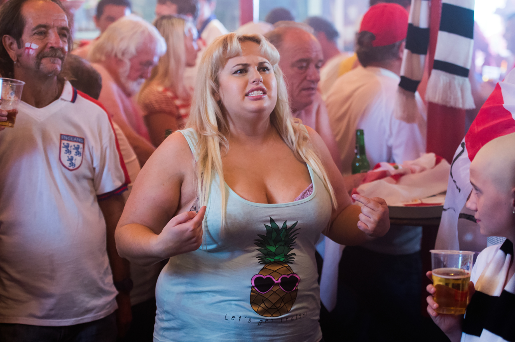 Woman in tank top with pineapple design among crowd of English football fans