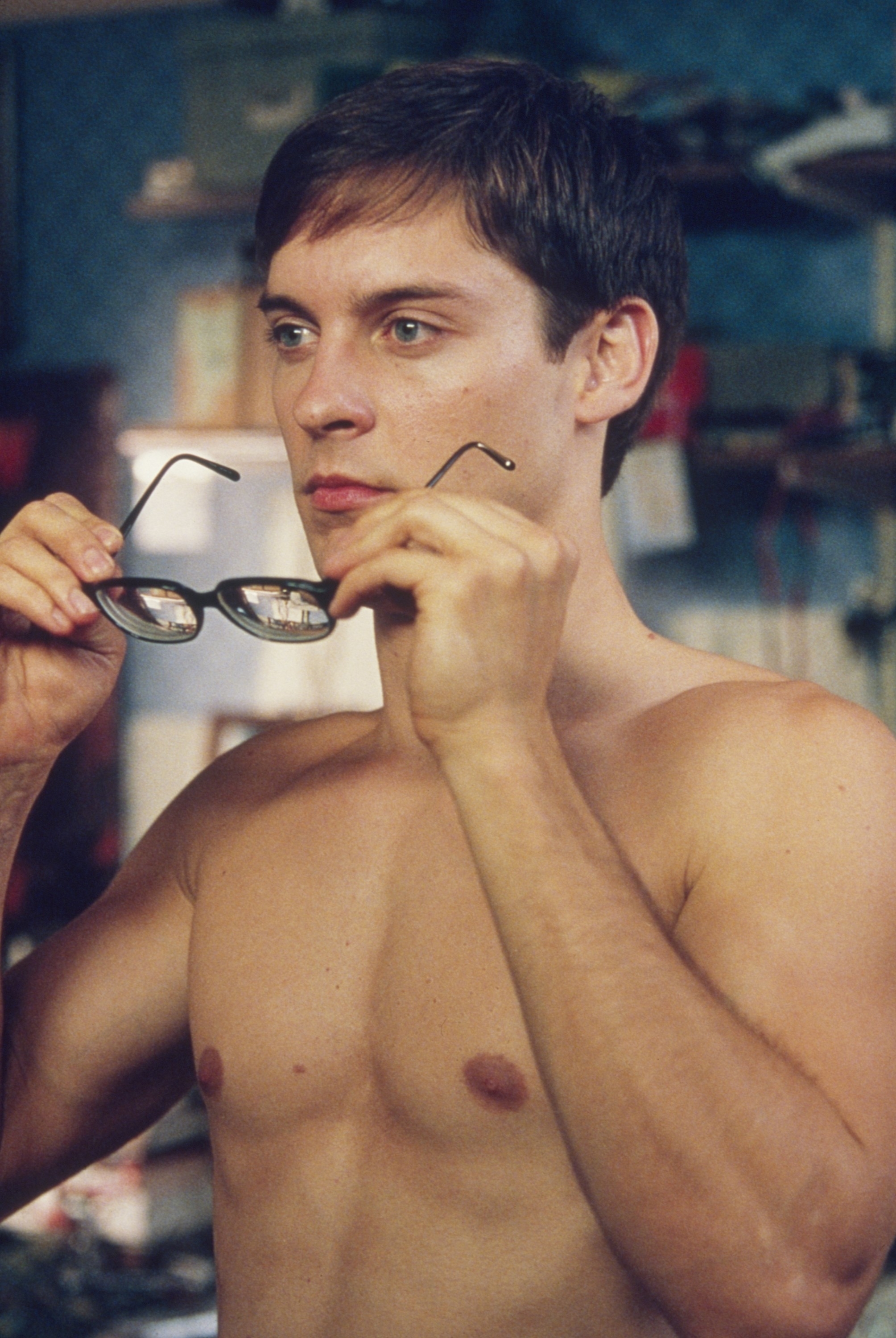 Tobey as Peter Park holding glasses up to face, shirtless, in an indoor setting