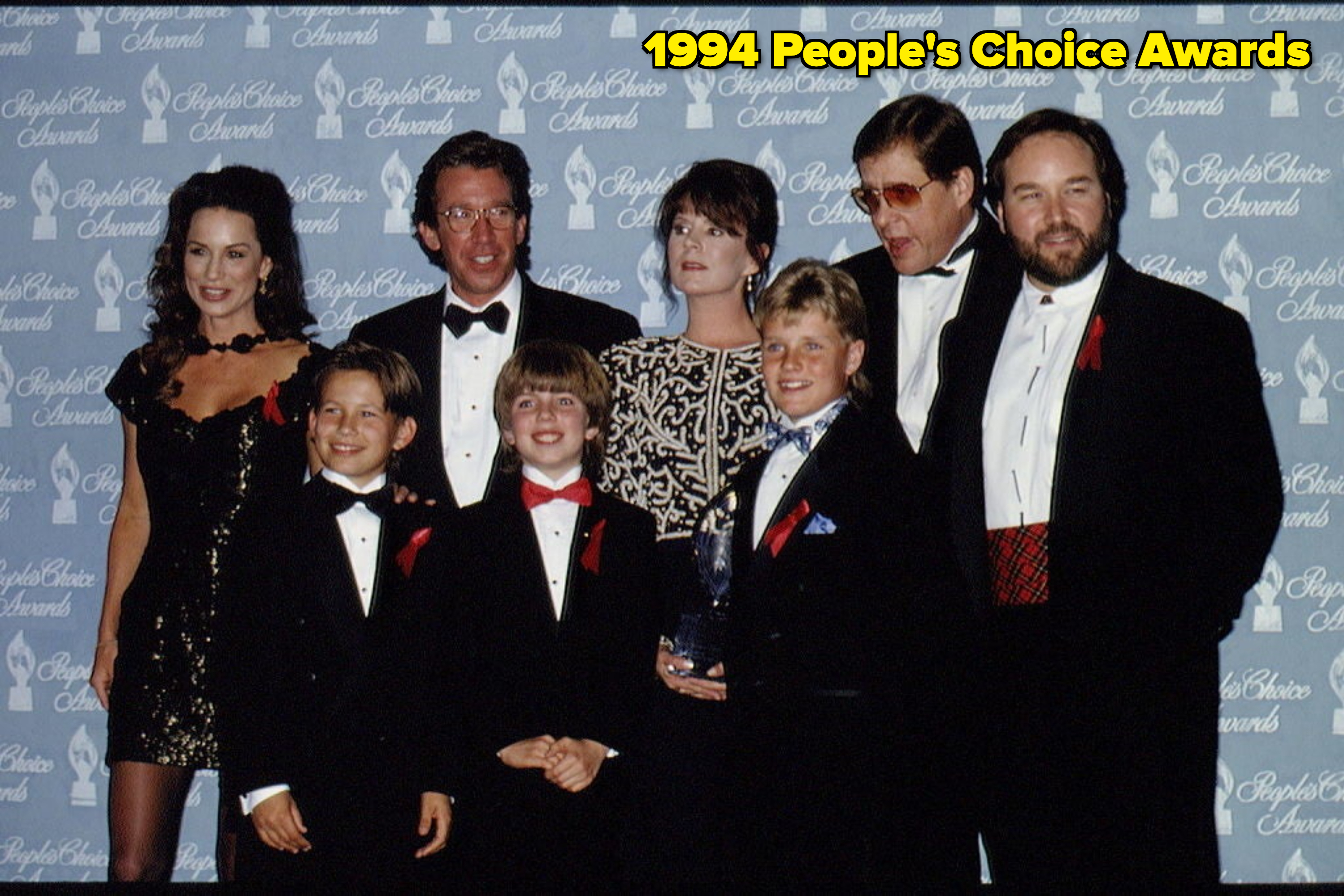 Group of seven at an award show; four adults in formal wear and three children in suits, with a trophy