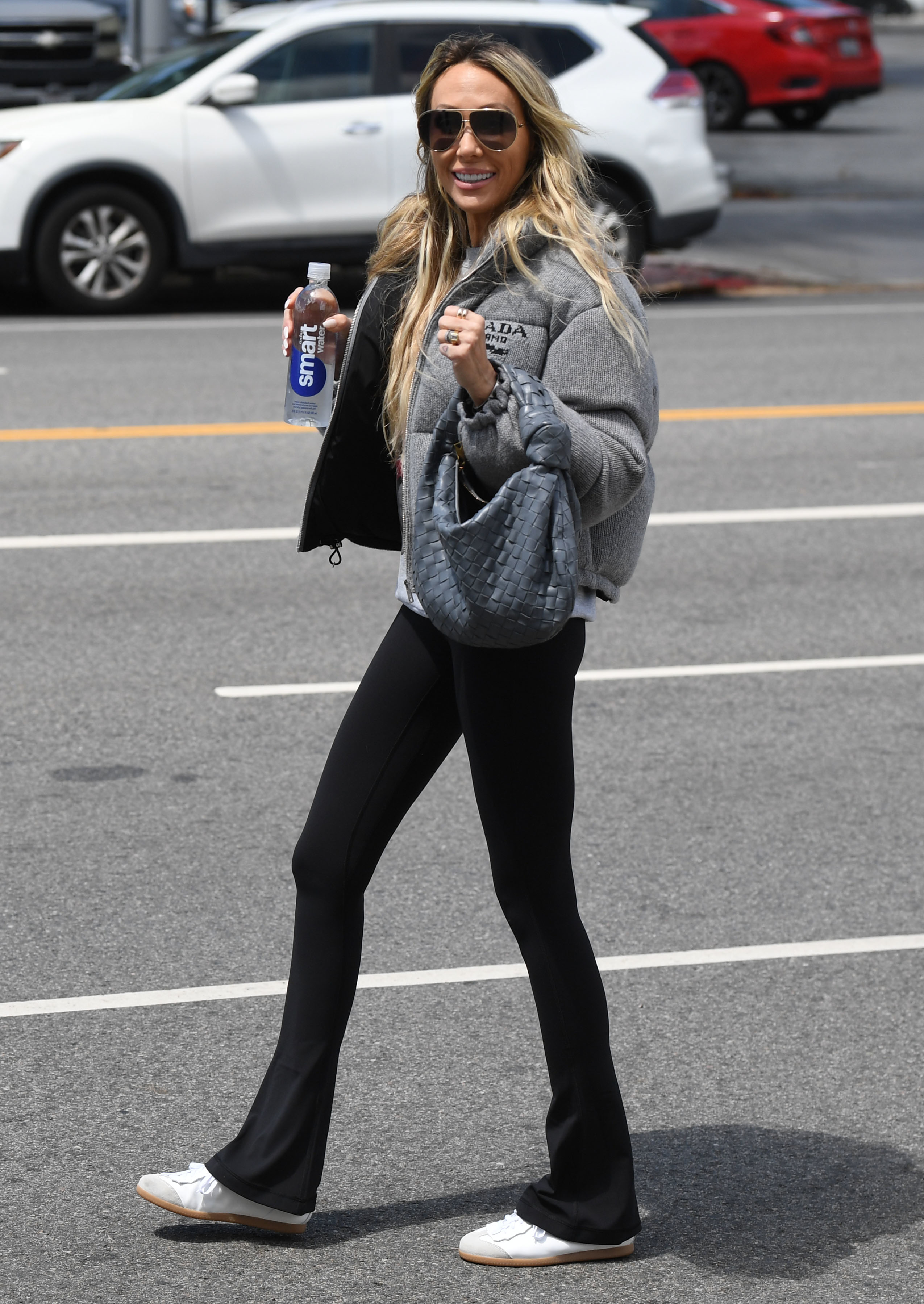 Woman in casual clothing with sunglasses, holding a water bottle, walking on a street