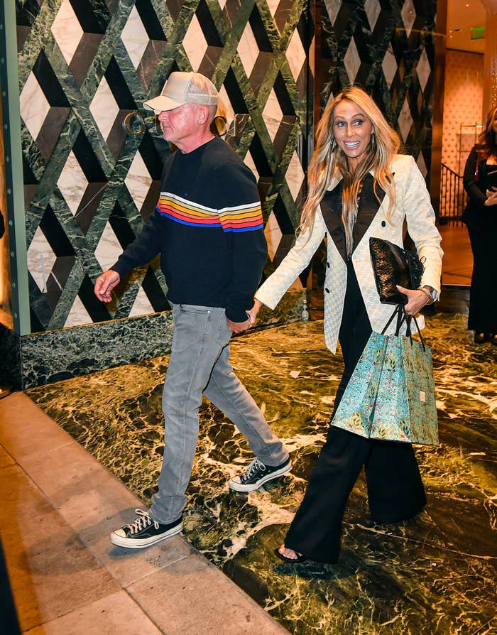 Two people walking side by side, man in sweater and jeans, woman in printed coat and flared pants, both smiling
