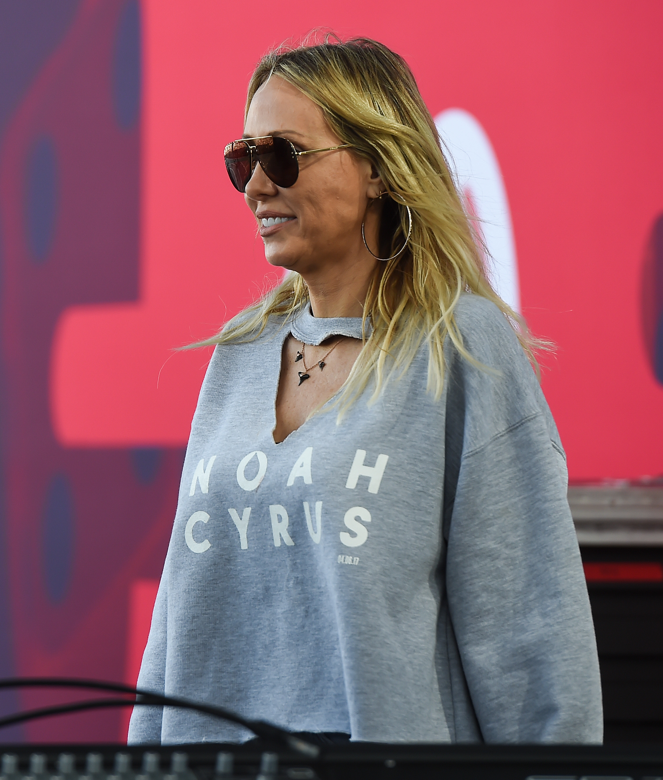Woman in sweatshirt with &quot;Noah Cyrus&quot; text, standing with microphone, outdoors