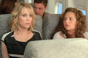 Two women seated next to each other on an airplane, appearing to have a conversation