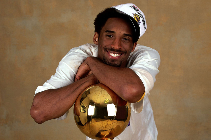Smiling person holding a shiny basketball trophy, wearing a white top and championship cap