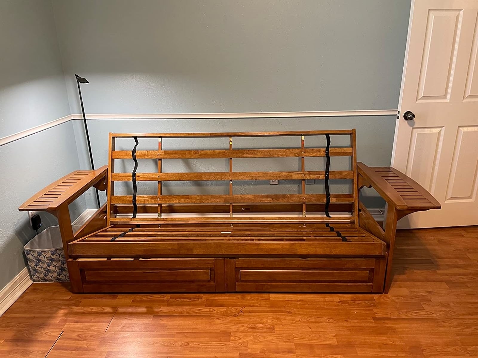 Wooden futon frame with side trays in a room, convertible into a bed, suitable for small spaces