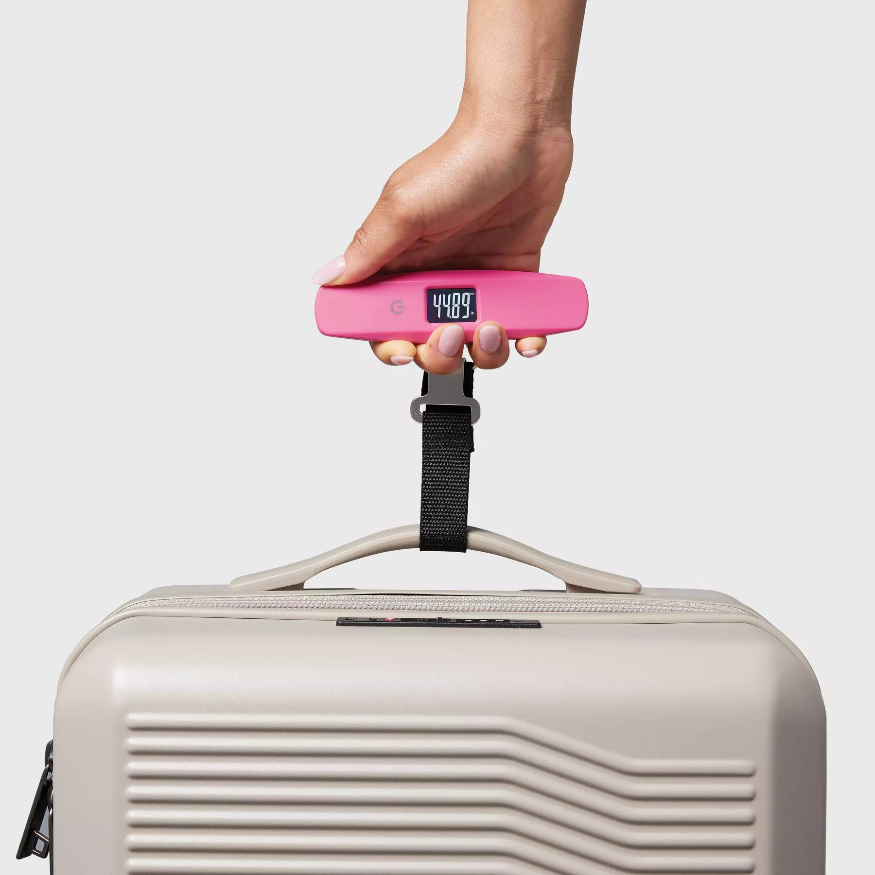 Hand holding a digital luggage scale with a reading, attached to a suitcase handle for weight measurement