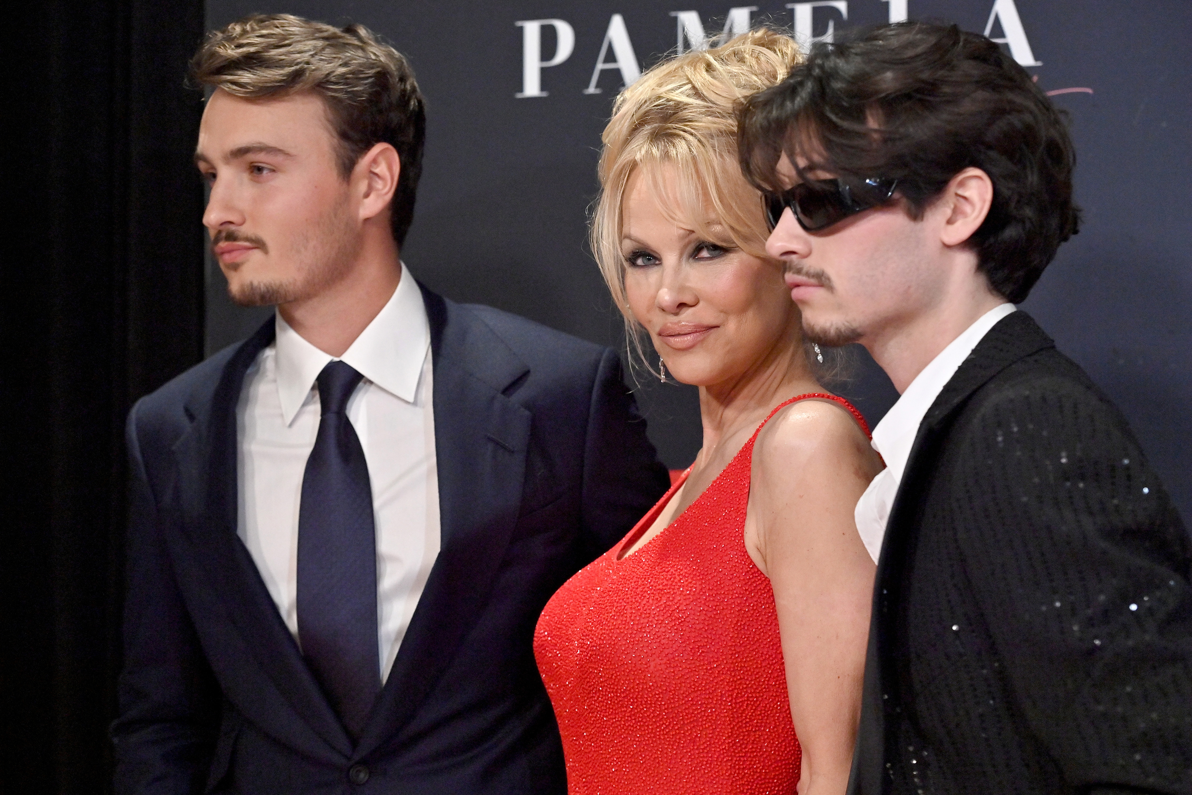 Pamela smiles on the red carpet with her adult sons flanking her