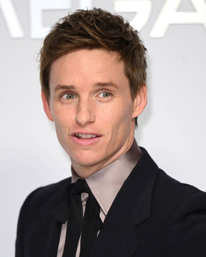 Eddie Redmayne in a suit with a tie, smiling at a formal event