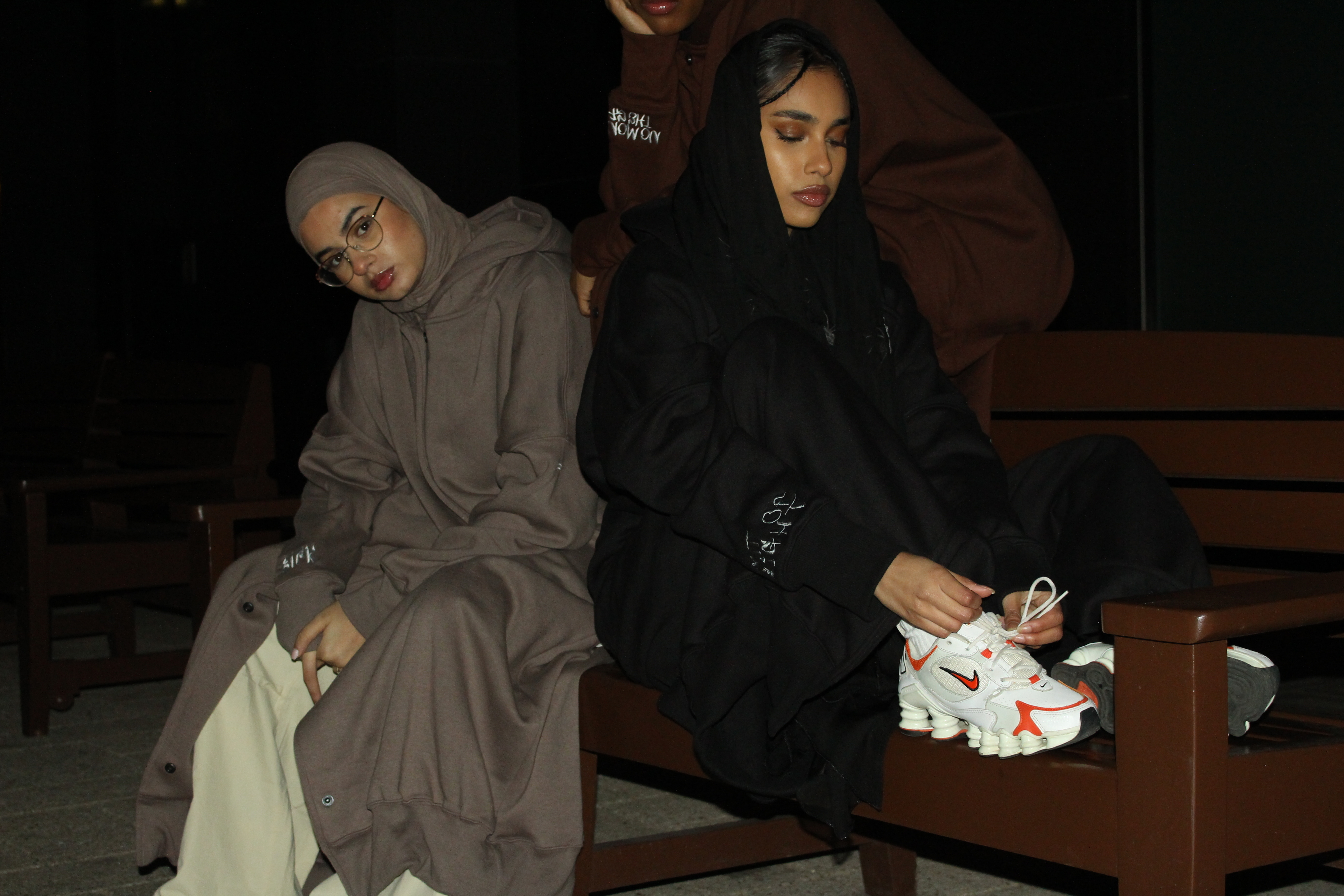 Two individuals in stylish modest fashion seated on a bench at night
