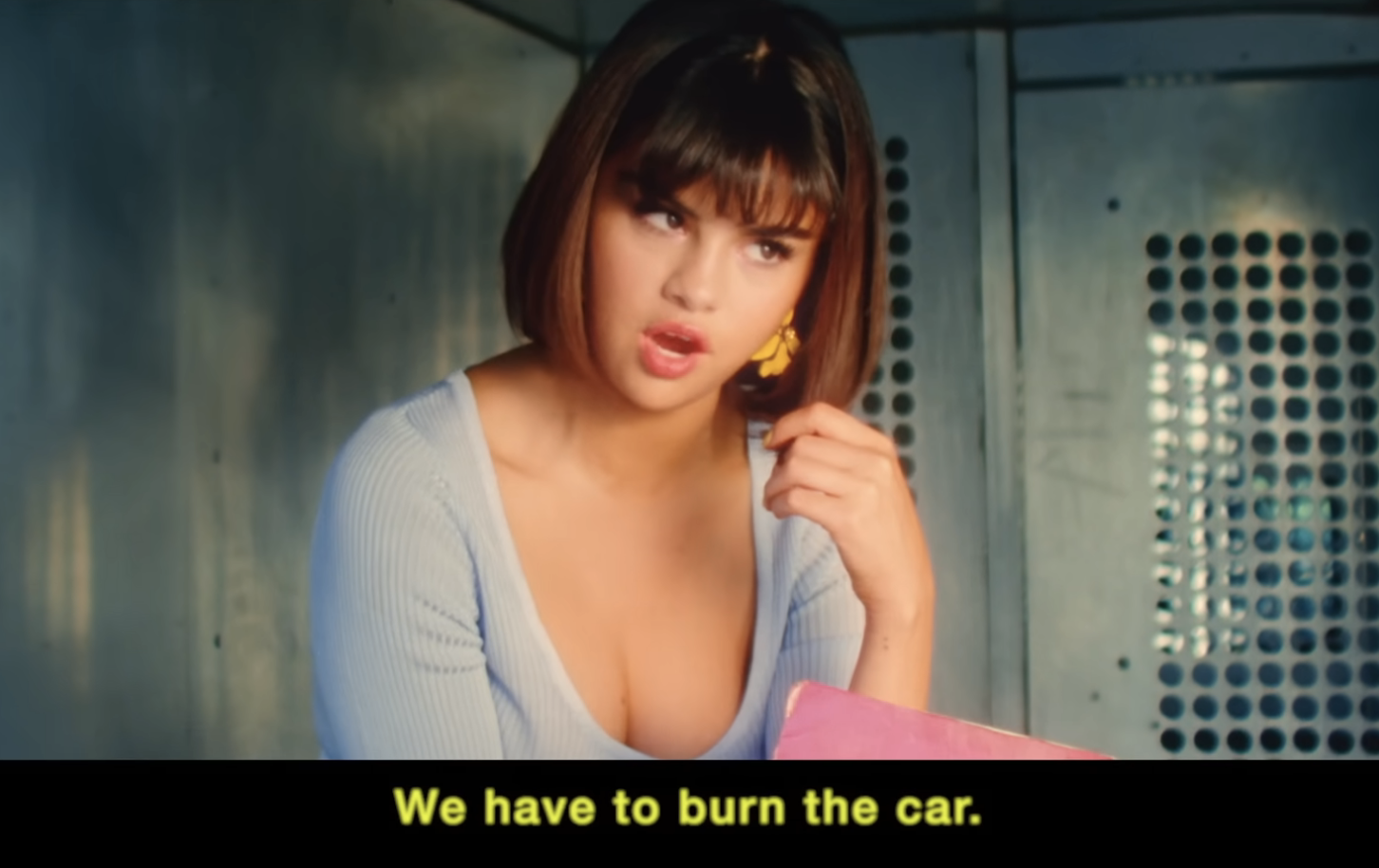 Selena Gomez in a music video scene, leaning against a car window with a vintage aesthetic and a lyric in a band along the bottom