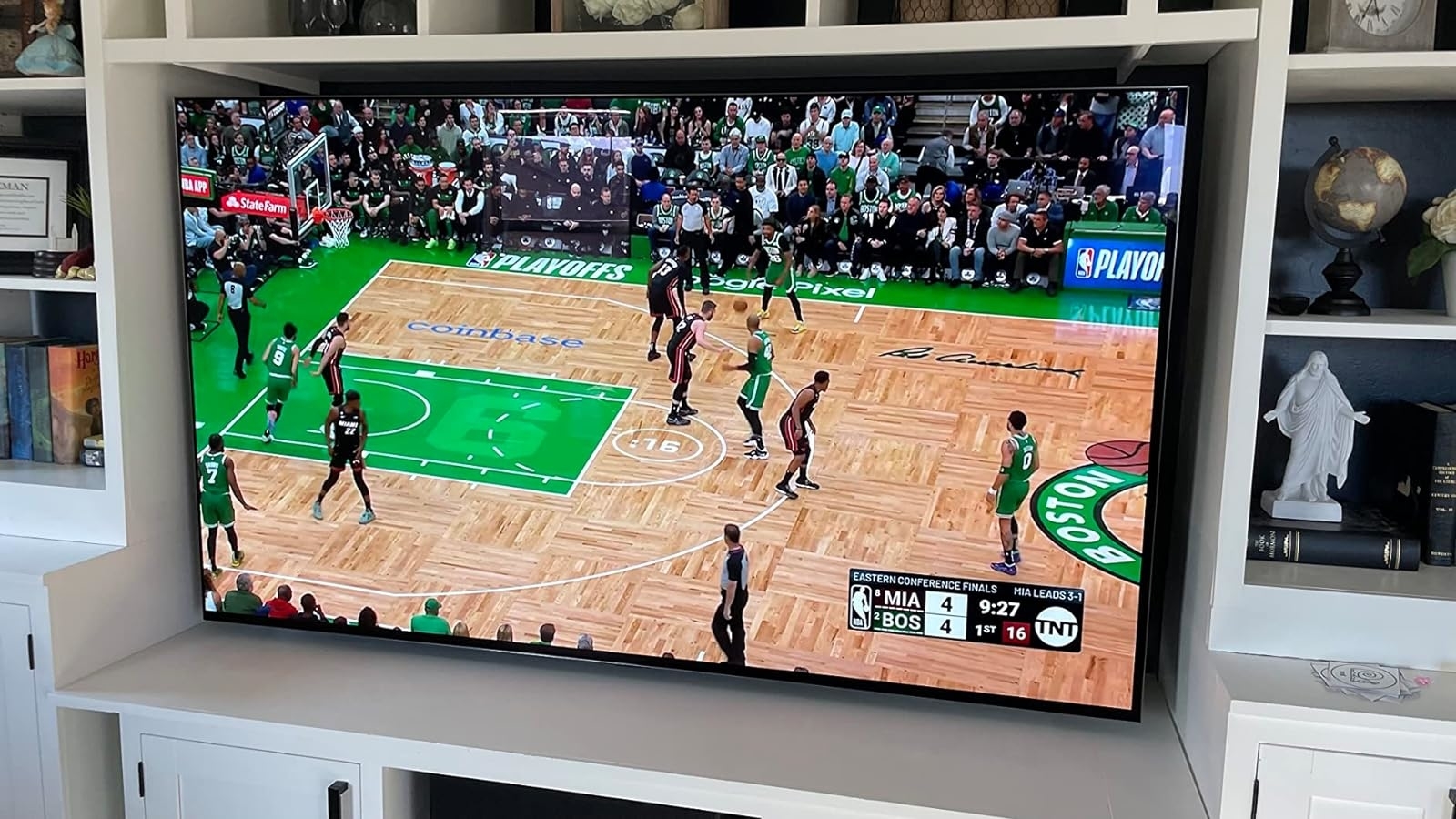 A TV screen showing a live basketball game between Miami and Boston teams, placed on a white entertainment center