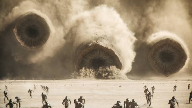 A dramatic still from the movie 'Dune: Part Two' with characters fleeing massive worms