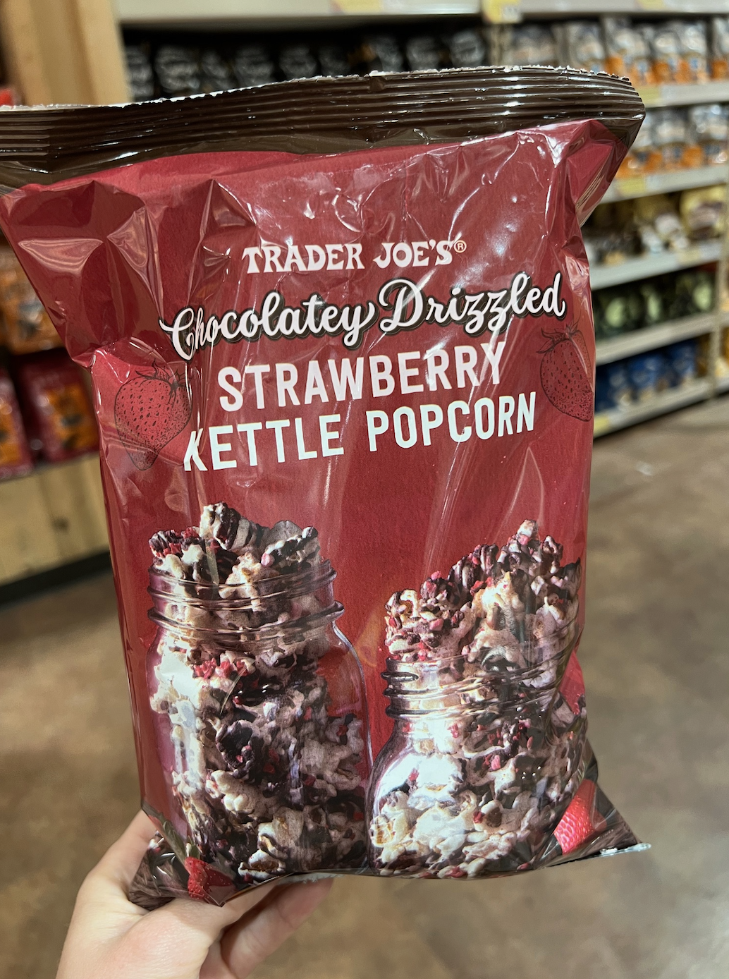 Hand holding a bag of Trader Joe&#x27;s Chocolatey Drizzled Strawberry Kettle Popcorn