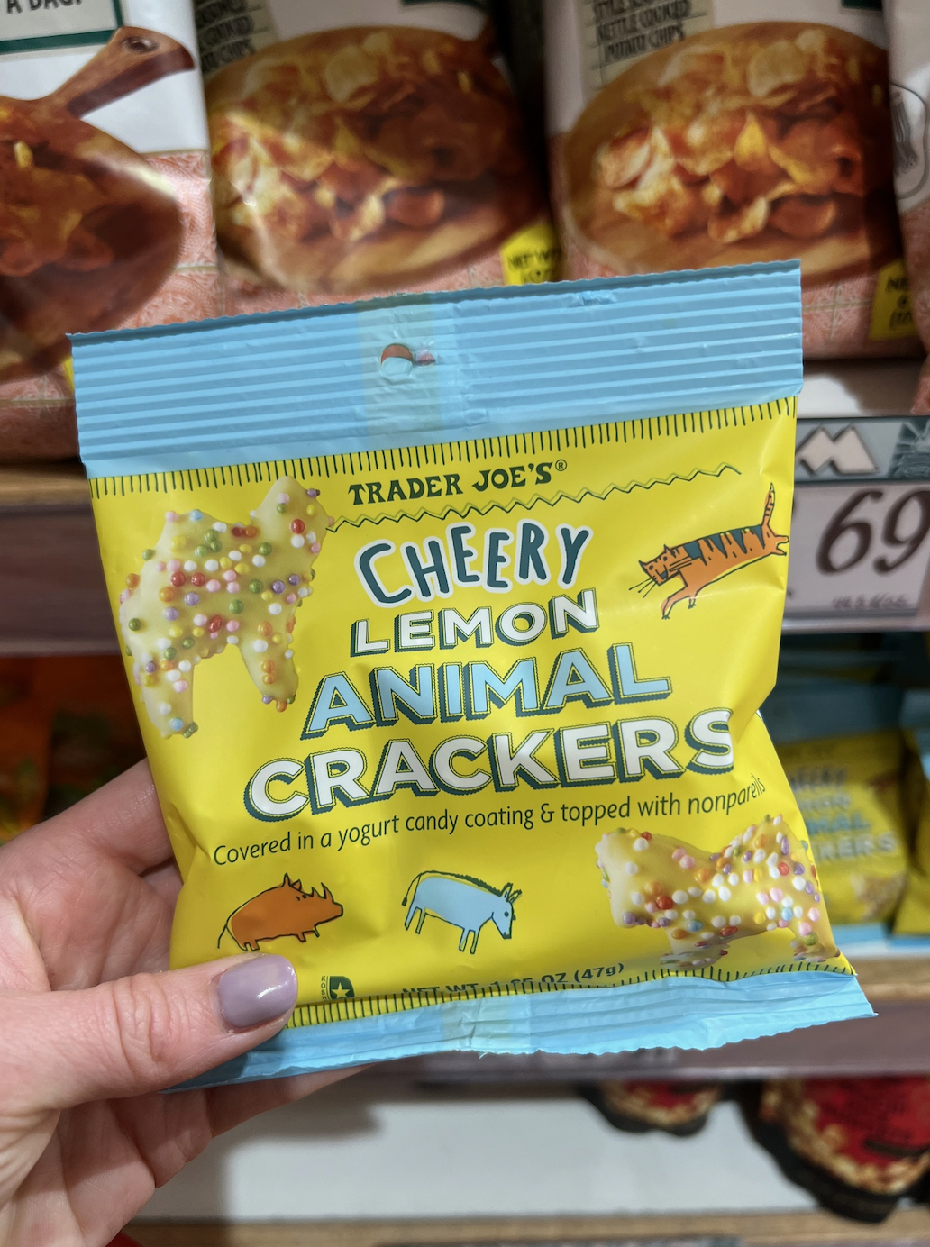 Hand holding a package of Trader Joe&#x27;s Cherry Lemon Animal Crackers in front of store shelves