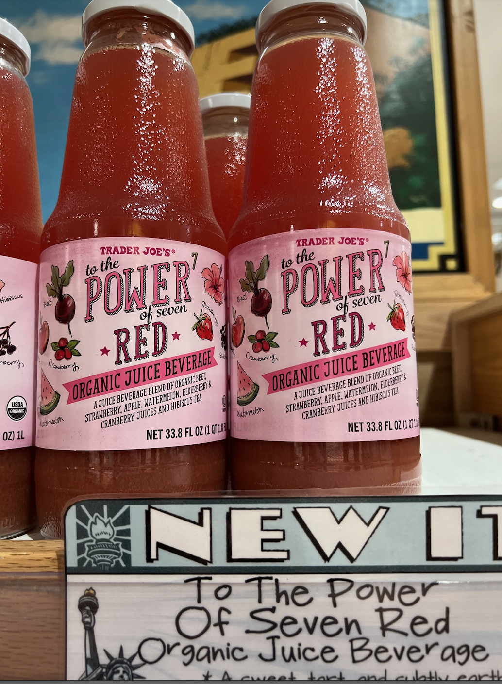 Sign and bottles labeled &quot;Trader Joe&#x27;s Organic Red Juice&quot; on a shelf, with &quot;NEW&quot; and description below