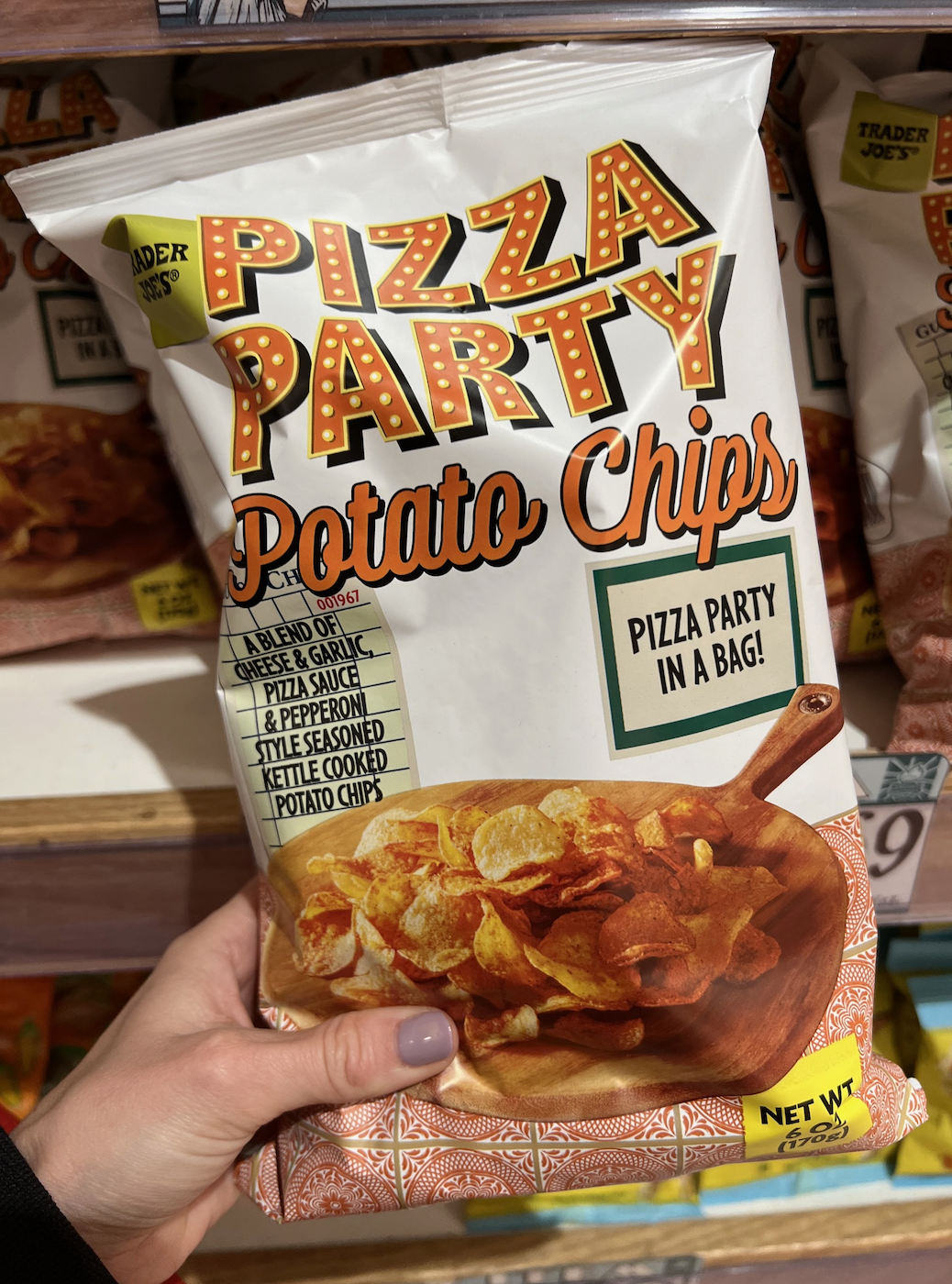 Hand holding a bag of Pizza Party Potato Chips with pizza-inspired flavors