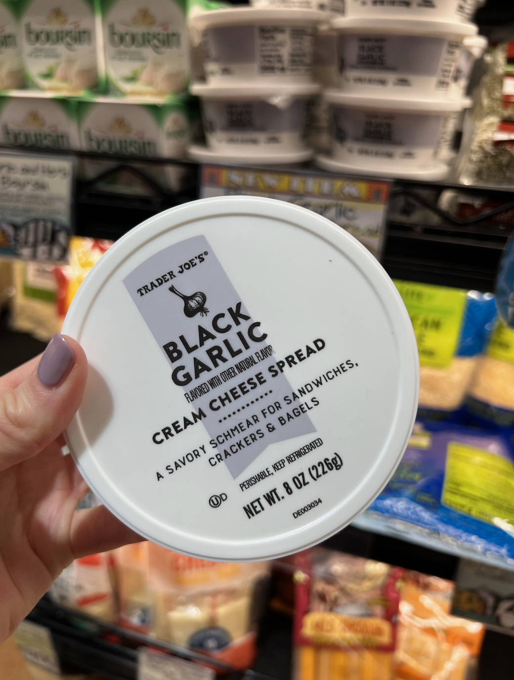 Hand holding a container of Trader Joe&#x27;s Black Garlic Cream Cheese Spread at a store