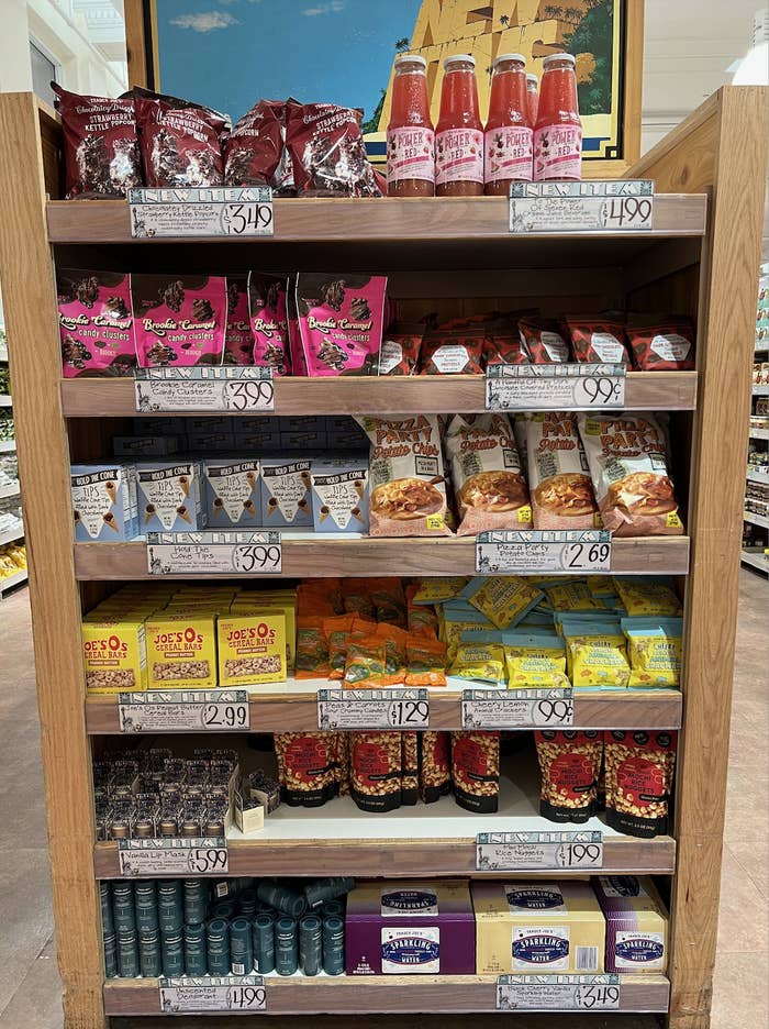 Grocery store shelf stocked with various food items including chips, bottled beverages, and baked goods.
