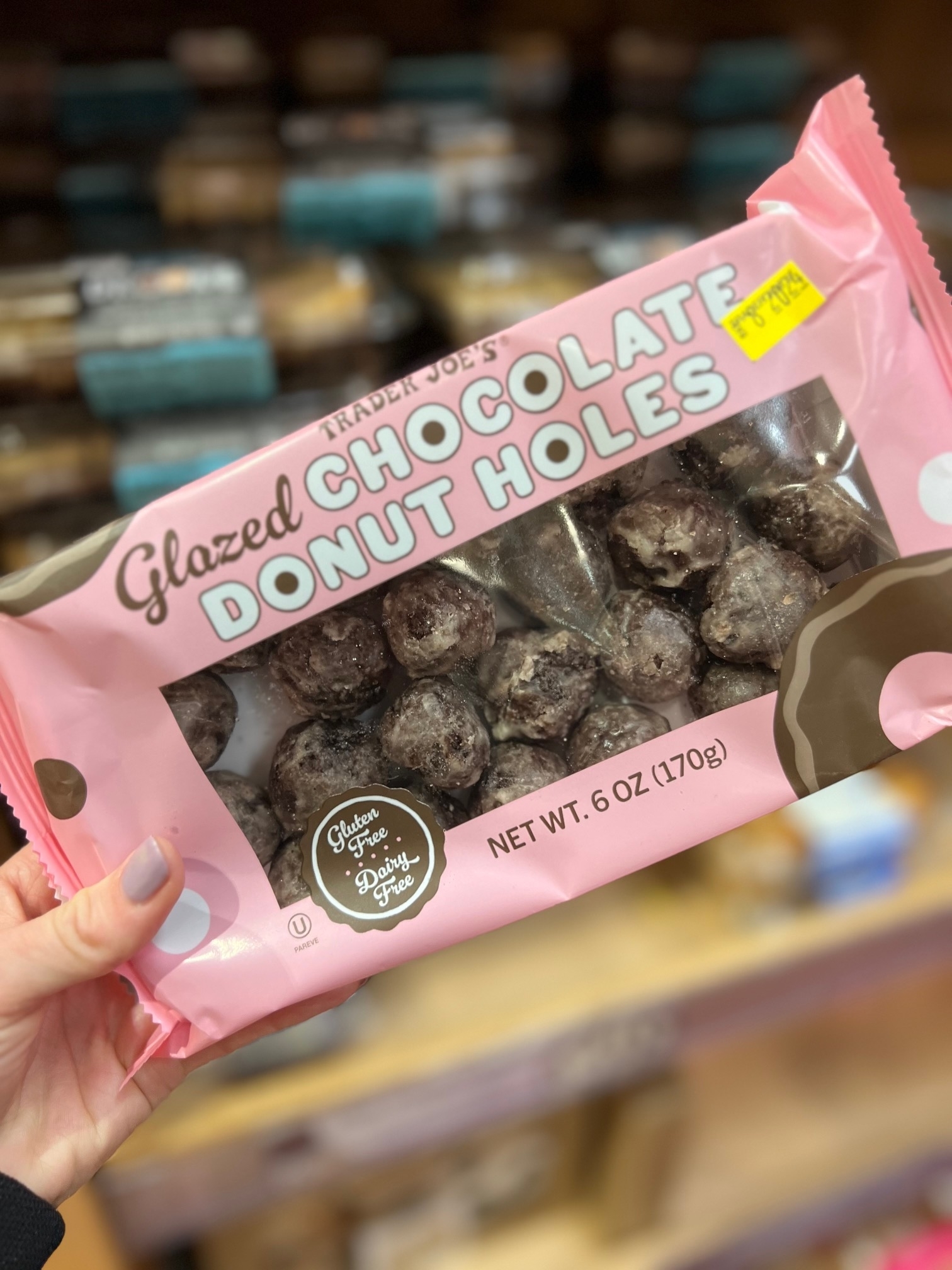 Hand holding a package of Trader Joe&#x27;s Glazed Chocolate Donut Holes on a store shelf