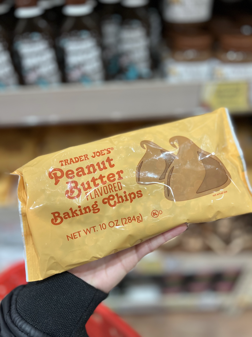 Hand holding a package of Trader Joe&#x27;s Peanut Butter Baking Chips in a grocery store aisle