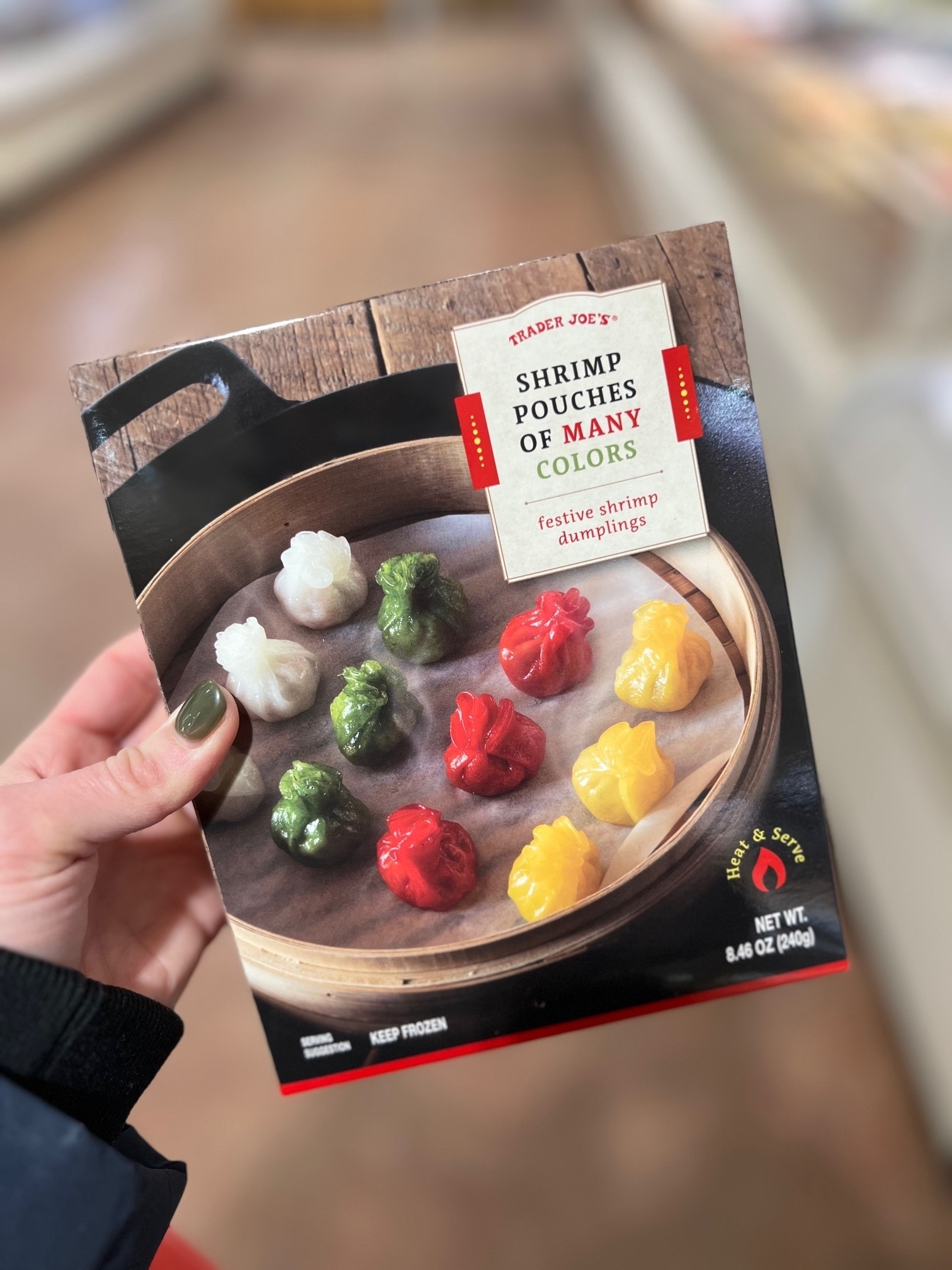 Hand holding a Trader Joe&#x27;s Shrimp Dumplings package with colorful dumplings displayed on a plate