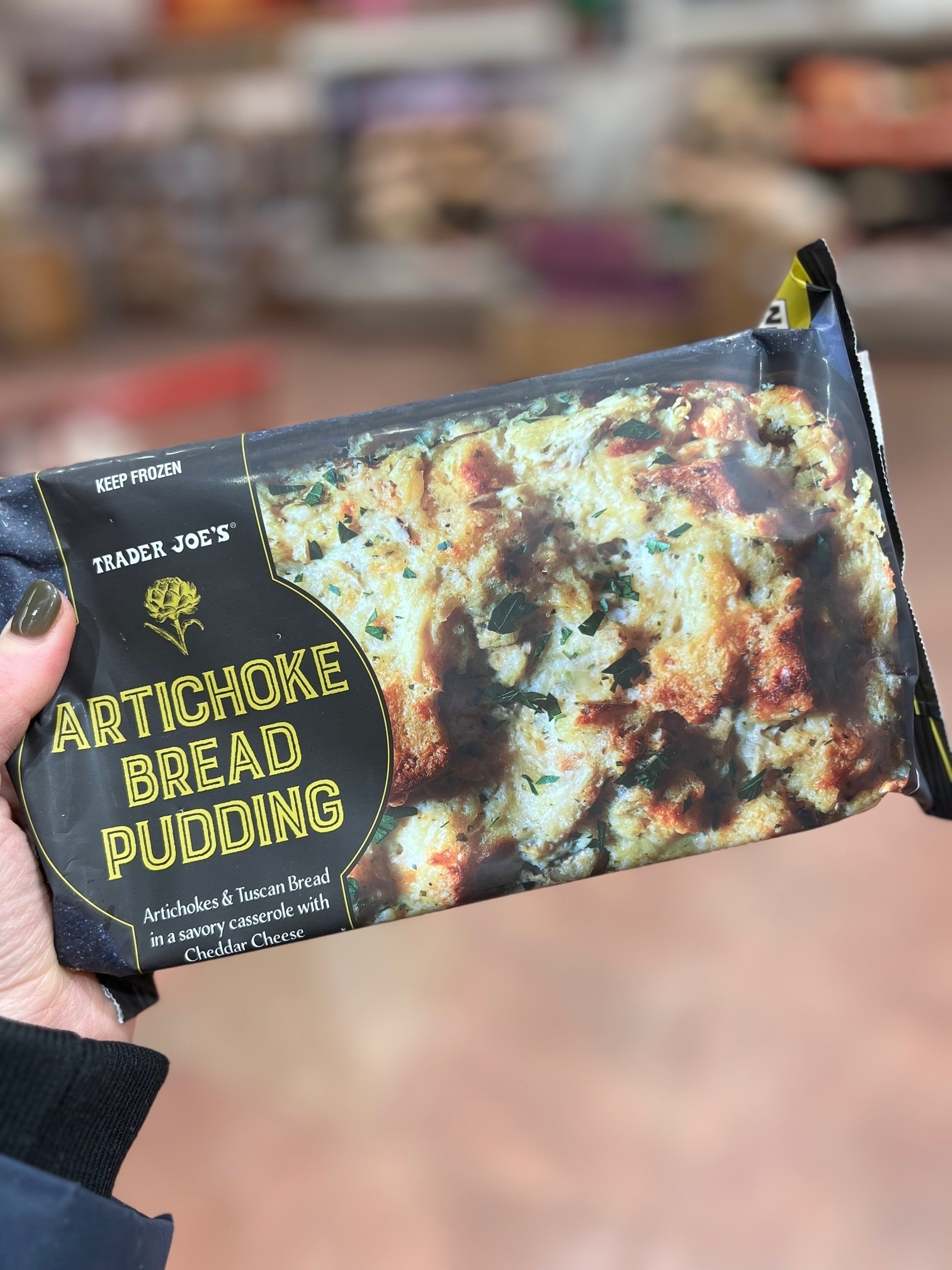 Hand holding Trader Joe&#x27;s Artichoke Bread Pudding package in a store