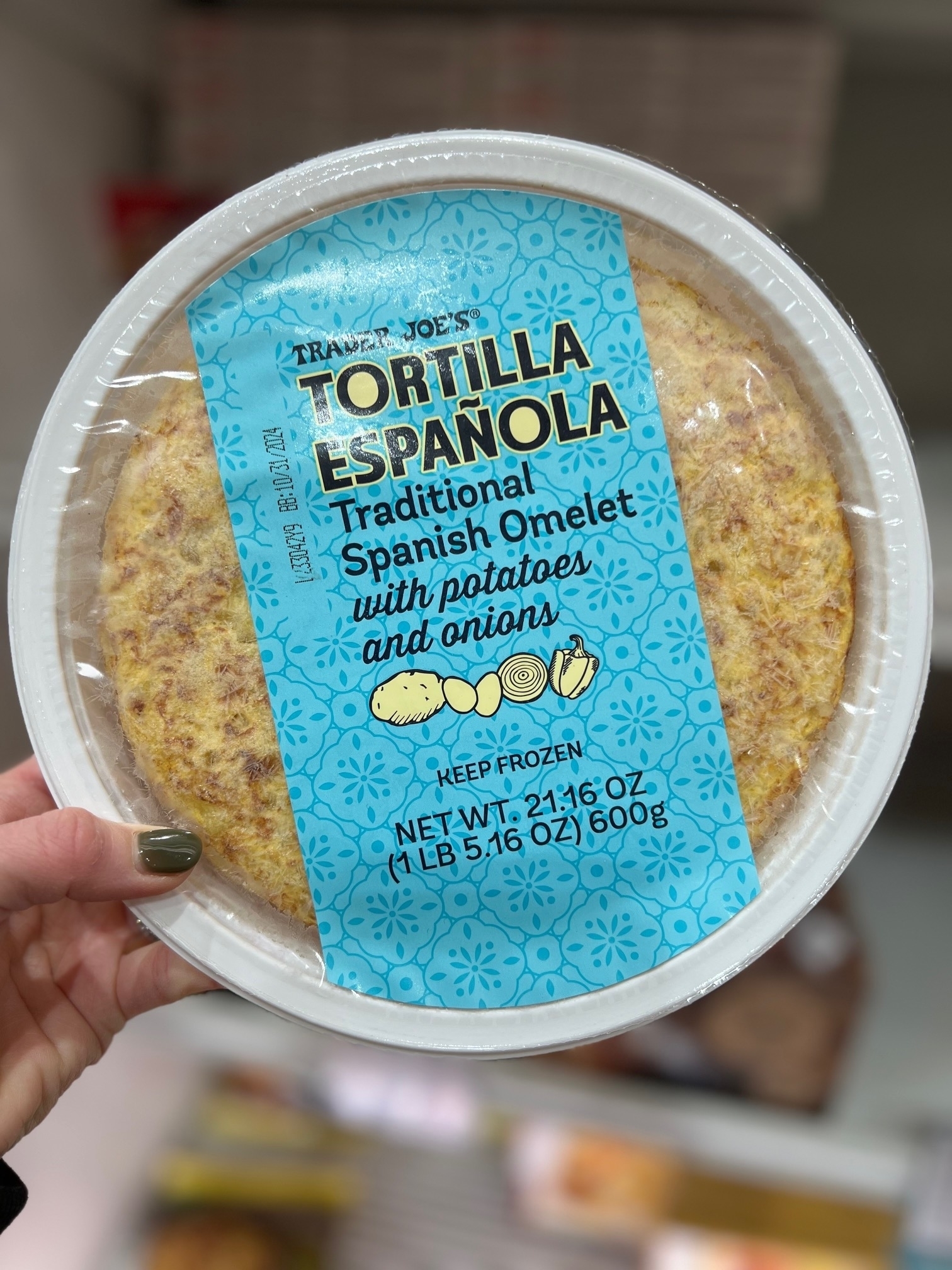 Hand holding a Trader Joe&#x27;s Tortilla Española Traditional Spanish Omelet packaging in a store