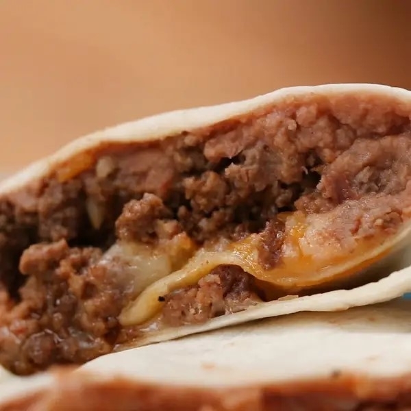 Close-up of a cheesy beef burrito cut in half, showing melted cheese and meat filling