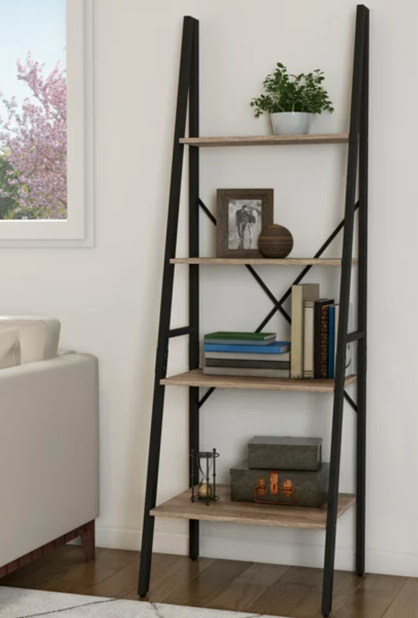 Five-tiered ladder-style bookshelf with assorted books and decorative items placed on it, situated next to a couch