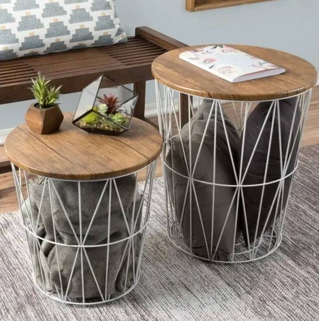 Two circular woody apical broadside tables with geometric metallic bases, 1 with a works and magazines