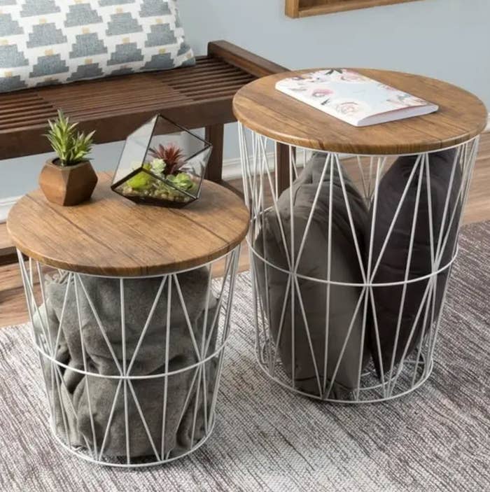 Two round wooden top side tables with geometric metal bases, one with a plant and magazines