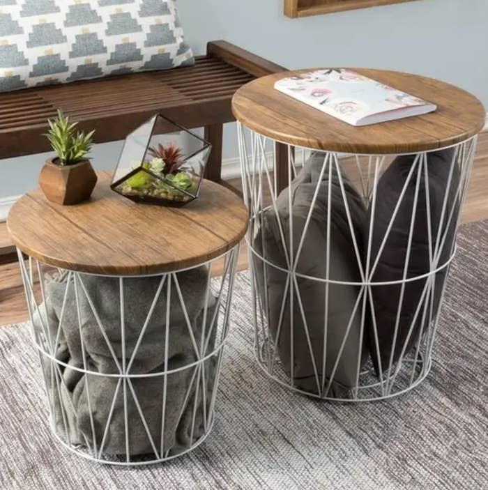 Two circular woody apical broadside tables with geometric metallic bases, 1 with a works and magazines