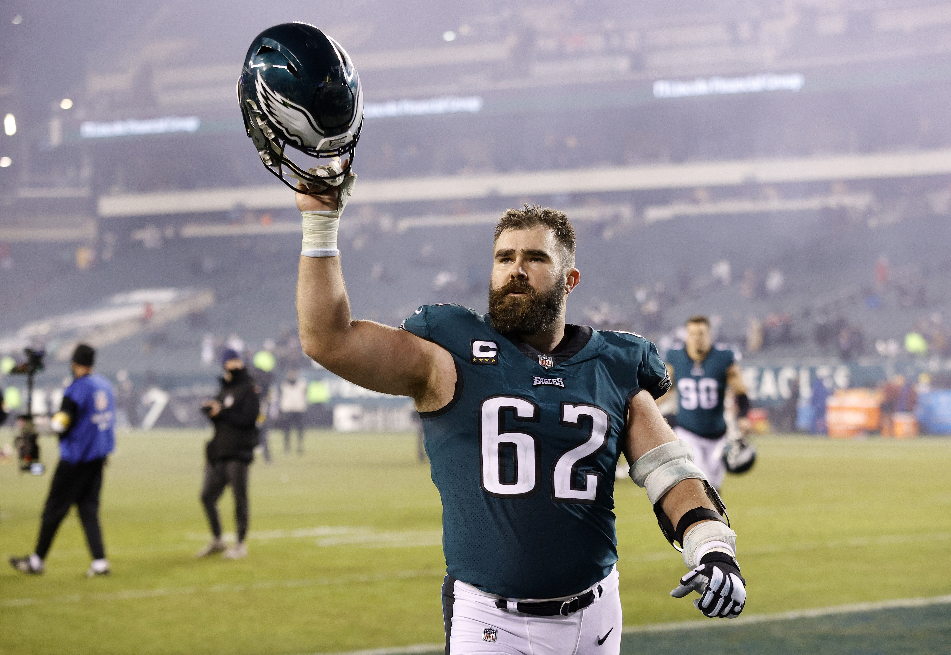 Jason Kelce on the field holding his helmet up in a victory gesture after a game