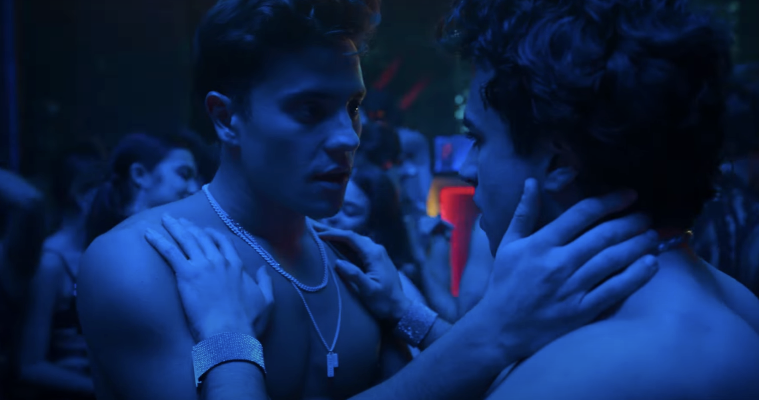 Two people are close and face each other intimately in a dimly lit, crowded setting, suggestive of a nightclub scene