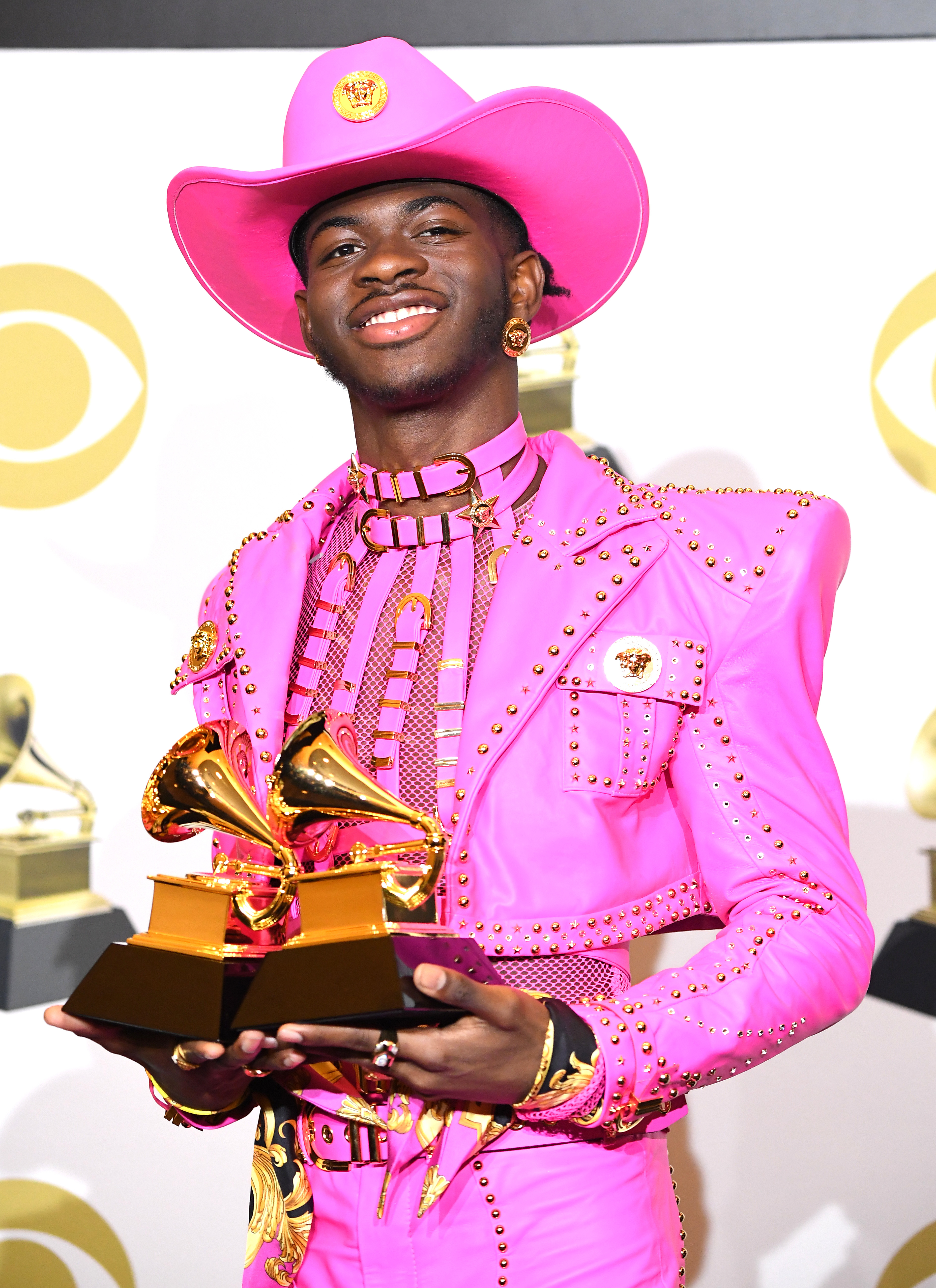 Lil Nas X in a vibrant pink cowboy outfit with gold details, holding Grammy Awards