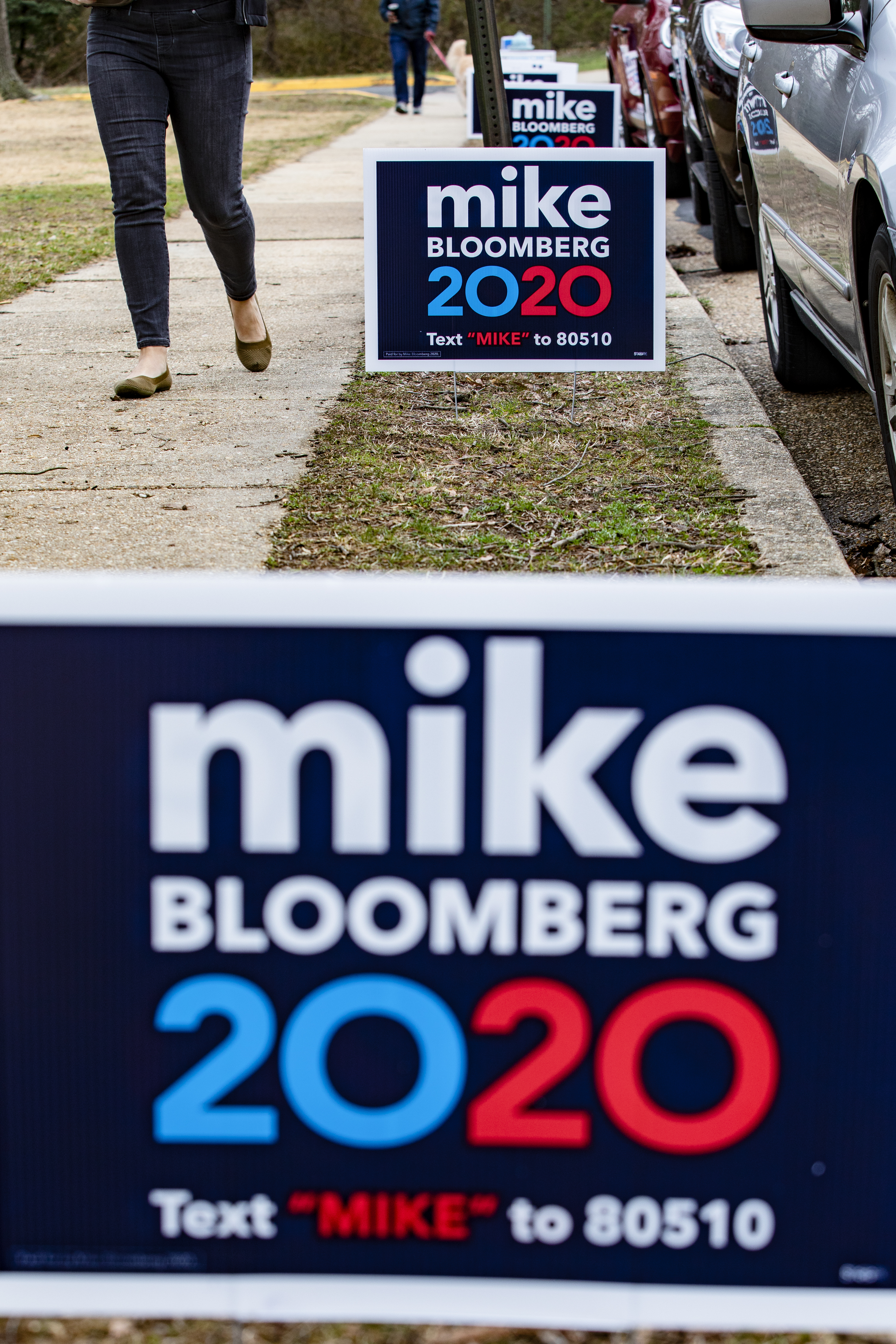 Person walking past &quot;Mike Bloomberg 2020&quot; campaign signs on a sidewalk
