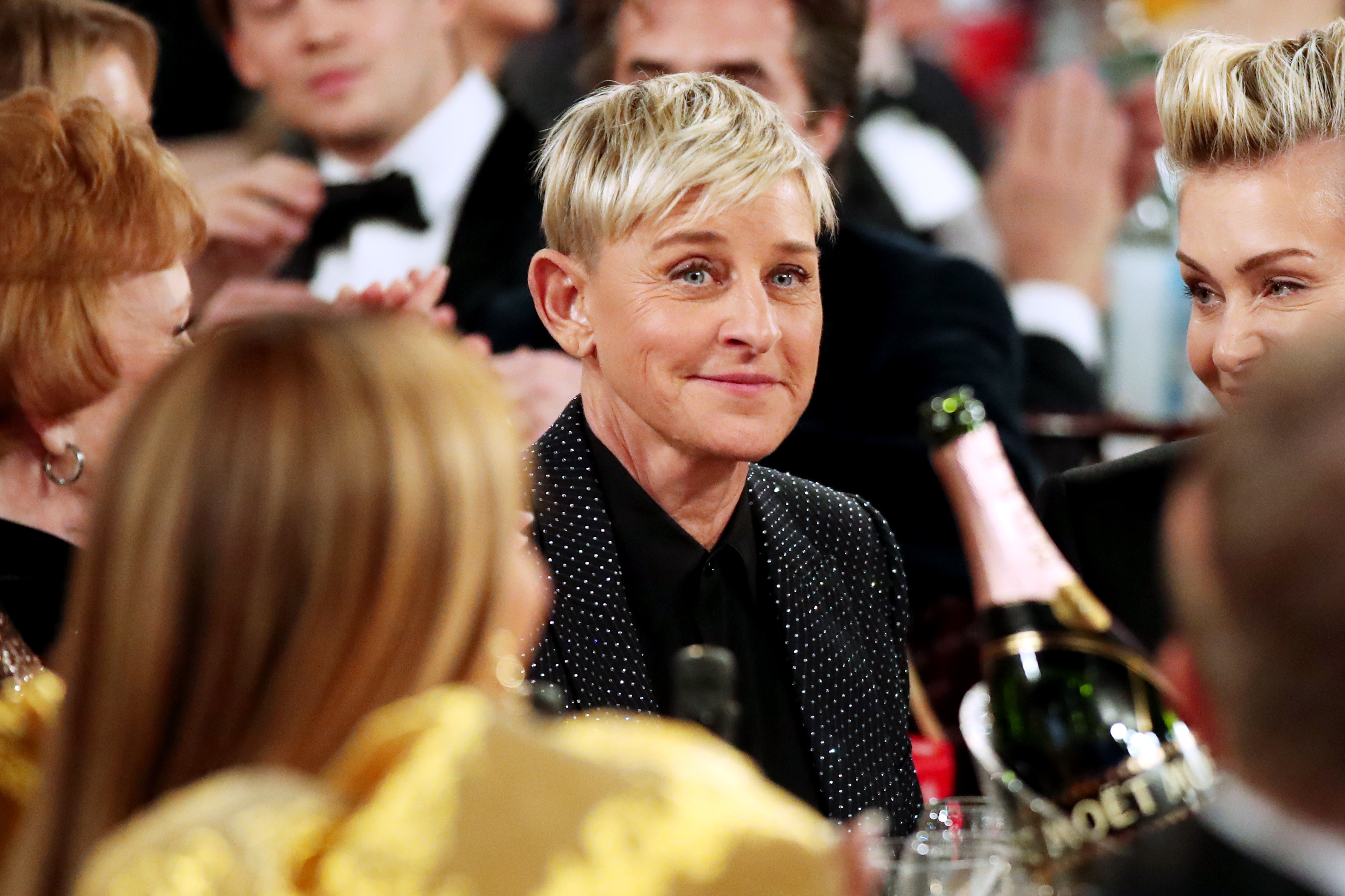 Ellen DeGeneres in a dotted suit at an event, surrounded by guests