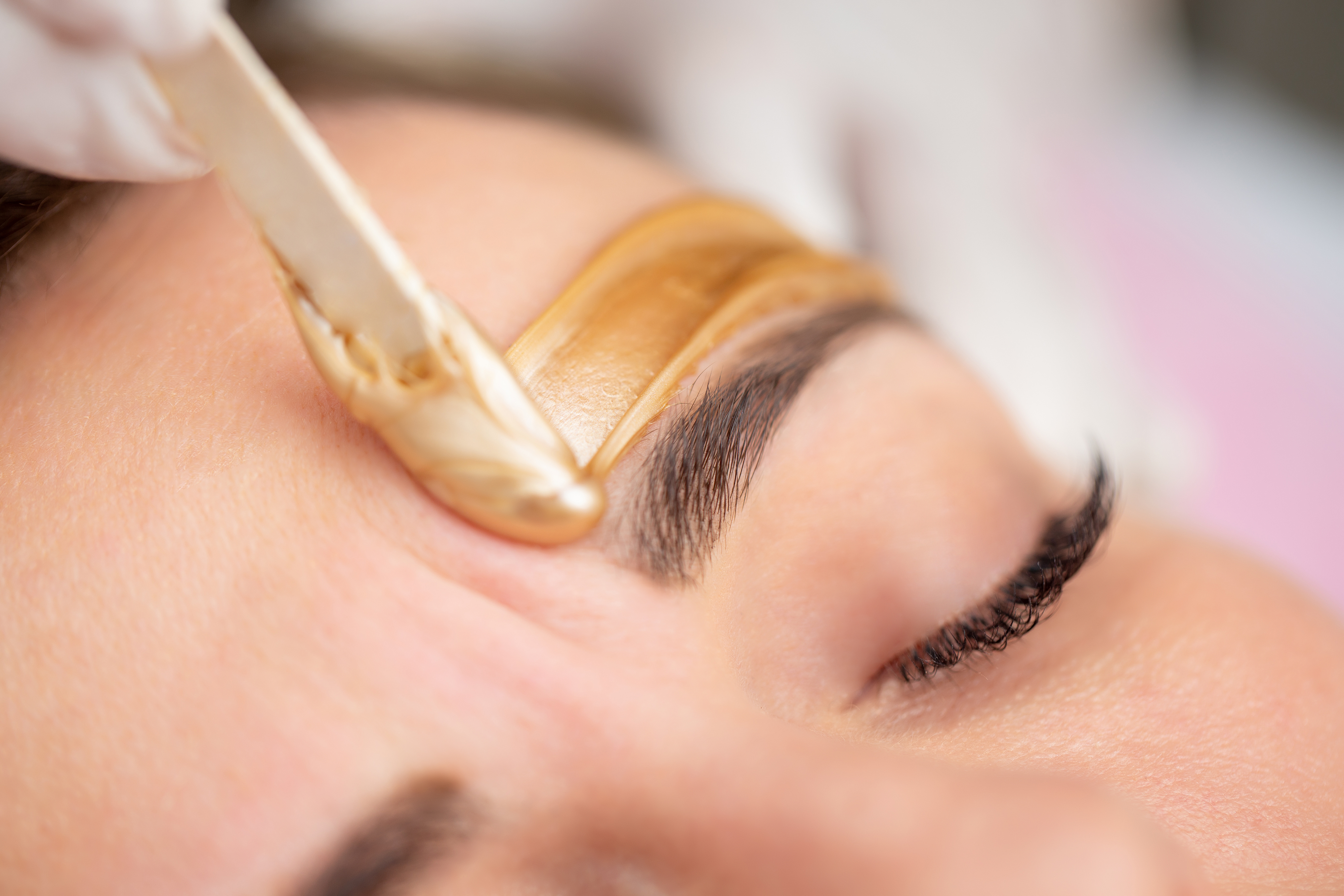Close-up of a person getting eyebrow wax applied, focusing on one eyebrow