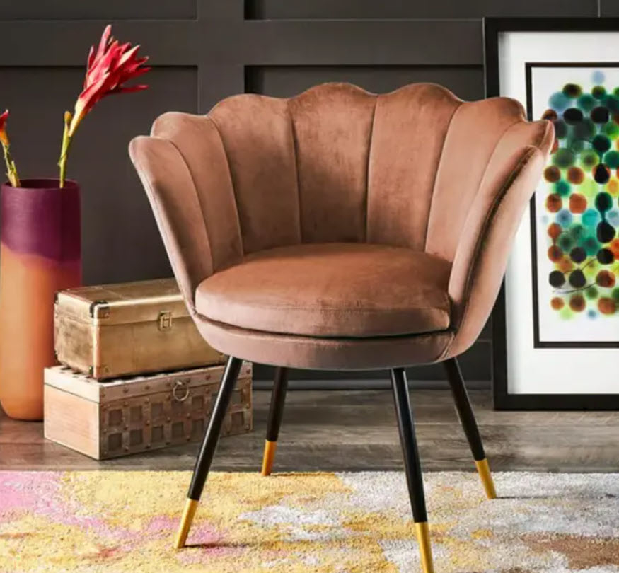 Elegant clamshell-style velvet chair with metal legs, next to a vintage suitcase, against a modern art piece