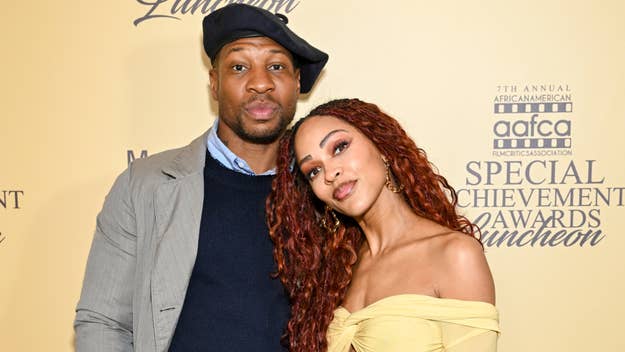 Jonathan Majors and Meagan Good posing at an event, one with a hat and blazer, the other wearing an off-shoulder dress