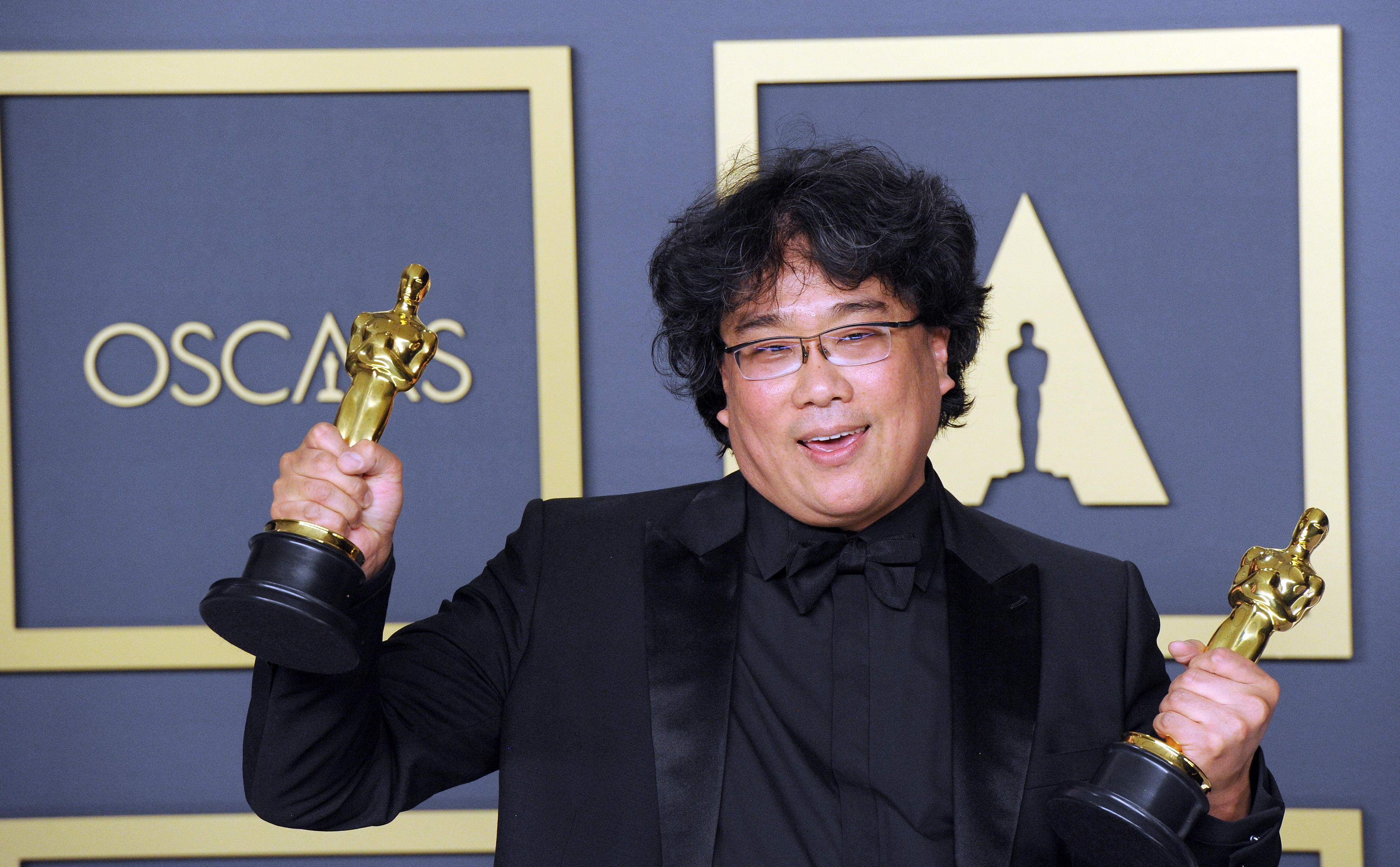 Director Bong Joon-ho in a black suit holds two Oscars