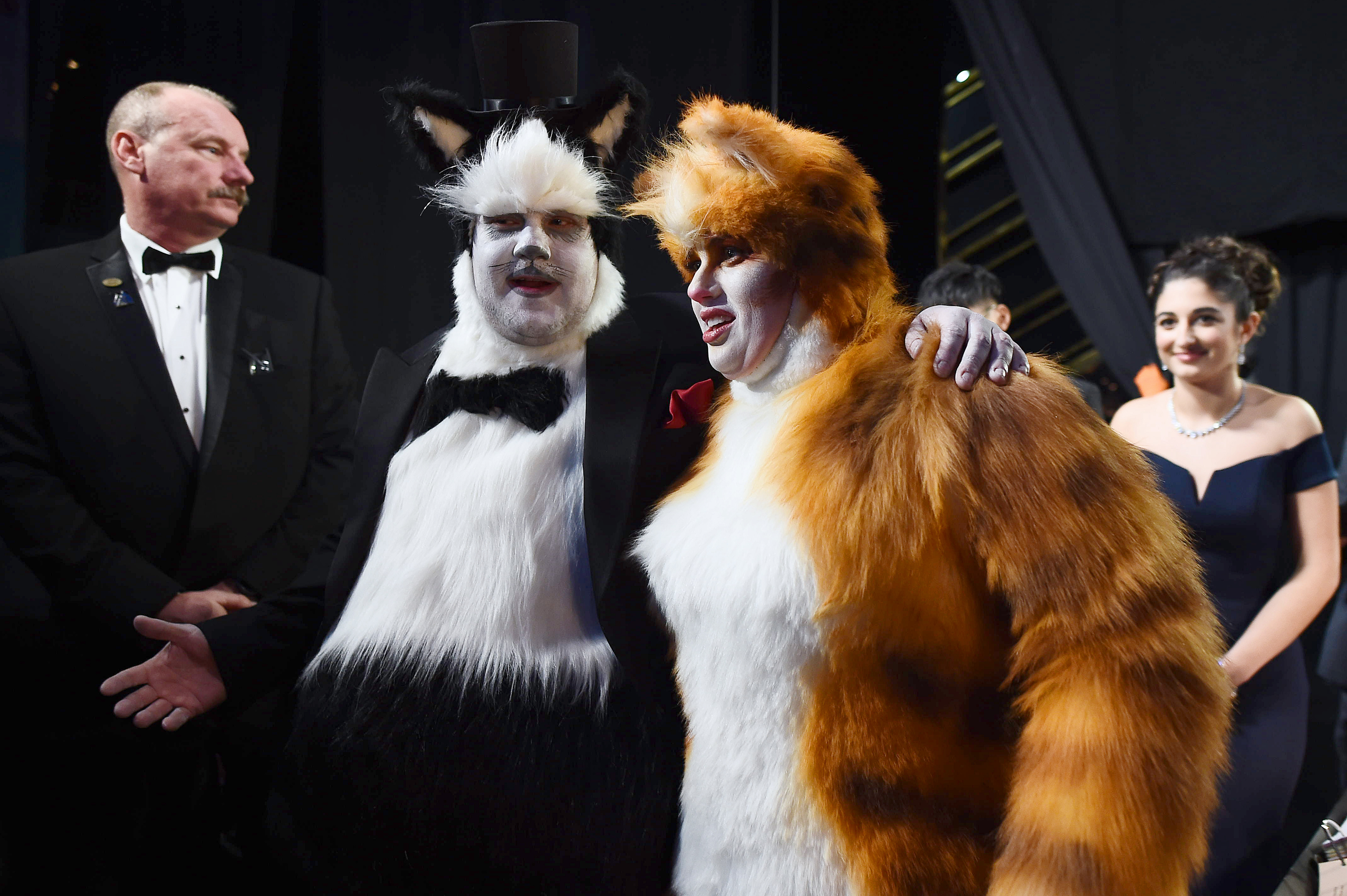 Two people in elaborate &quot;Cats&quot; musical costumes with theatrical makeup, posing with others at an event
