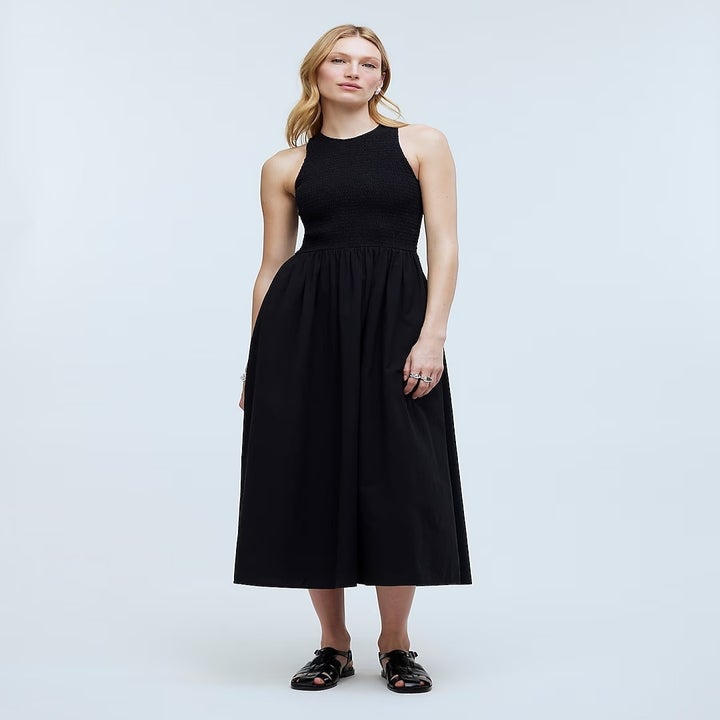 Model wearing a sleeveless black midi dress with a fitted top and flared skirt, paired with black loafers