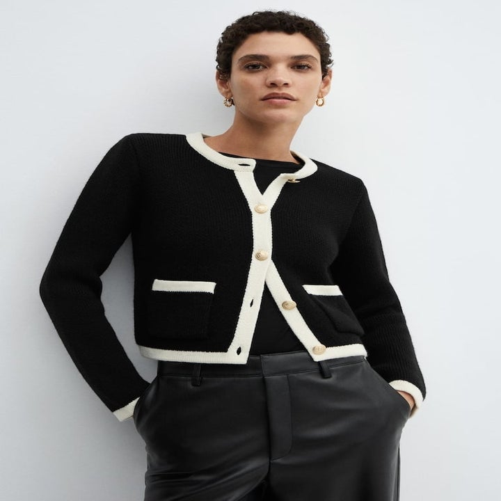 Model in a black cardigan with white trim and large buttons, paired with dark trousers, for a classic look