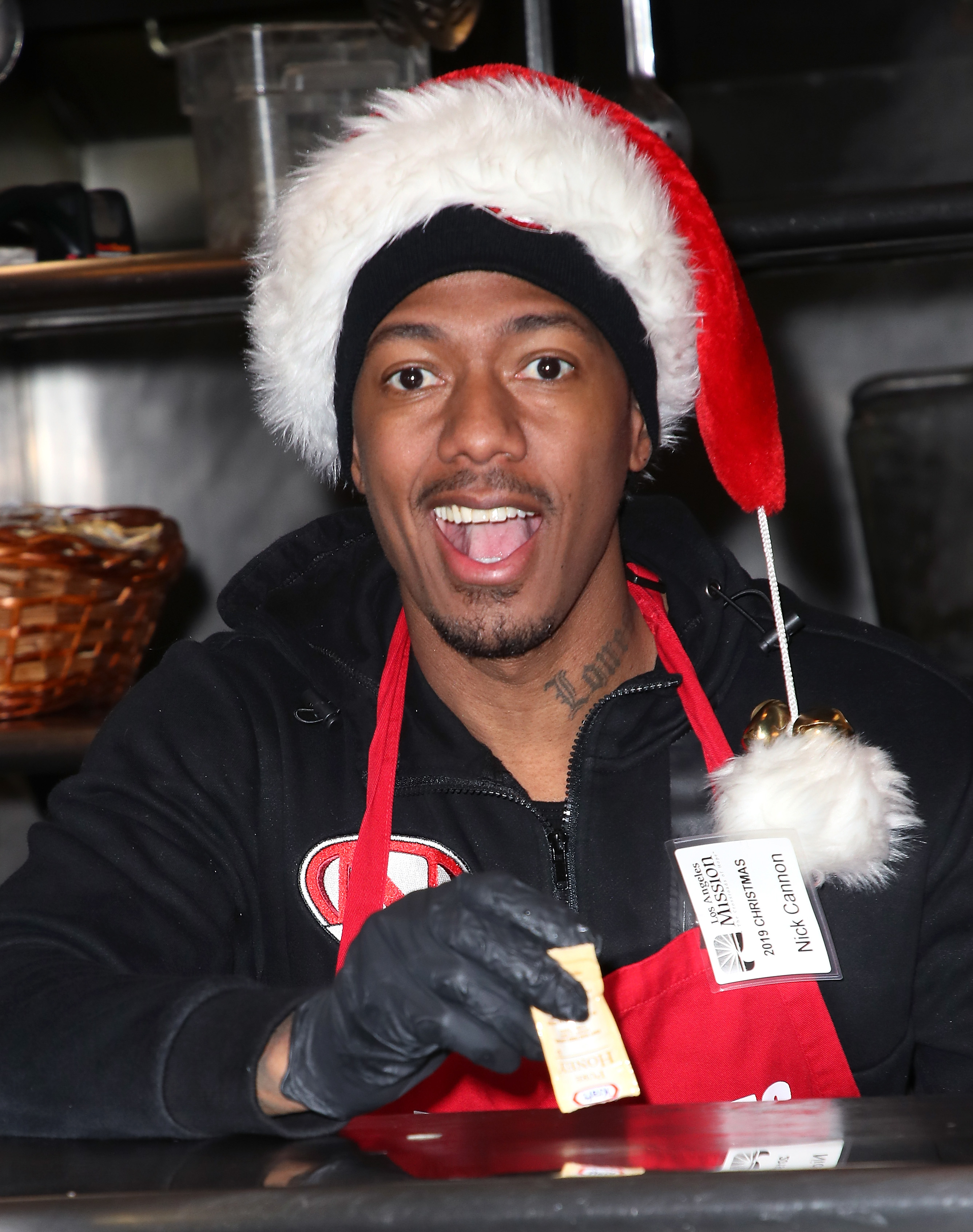 Nick in a Santa hat serving at an event, smiling, wearing a name badge and black gloves